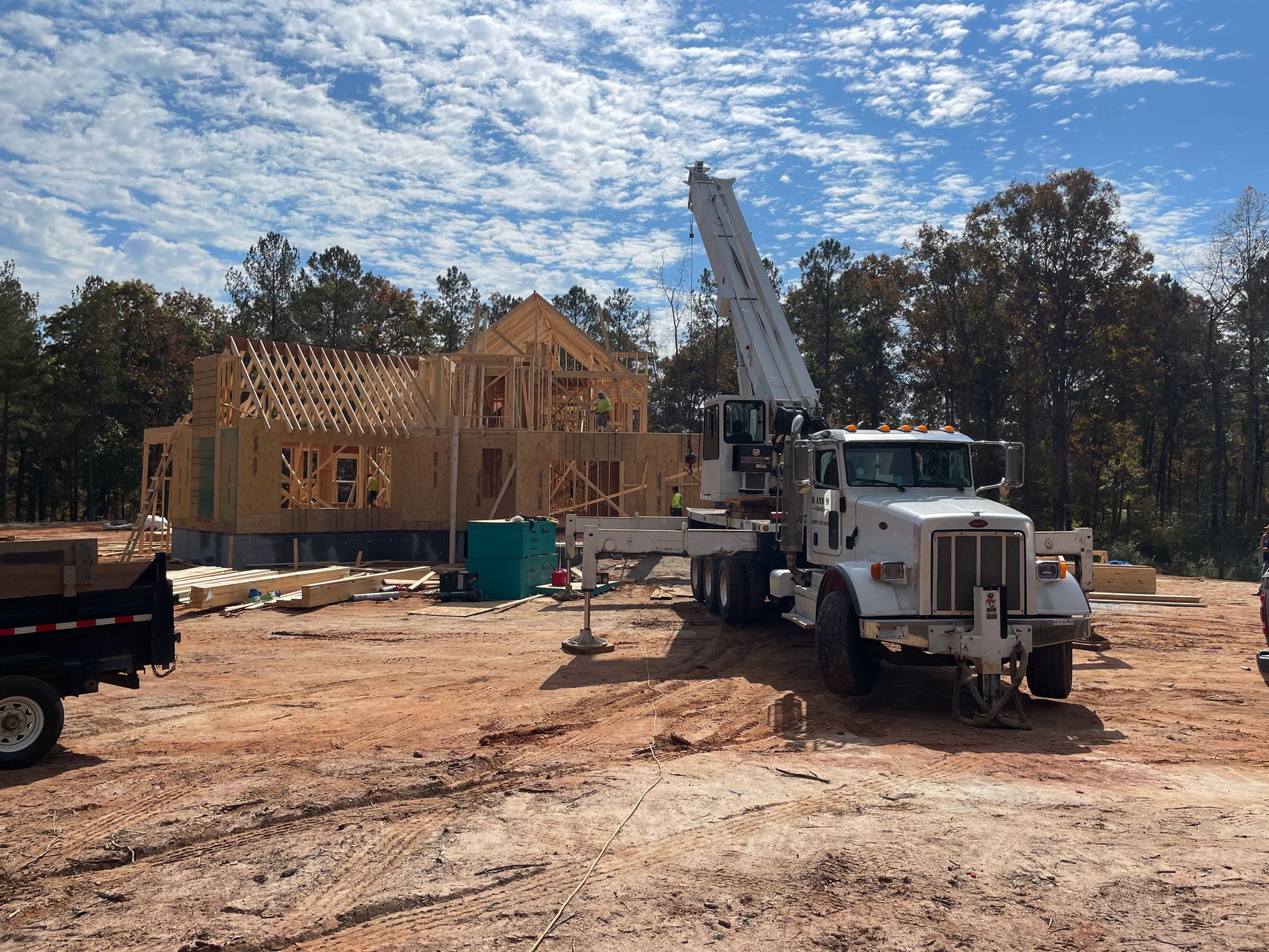 Construction site with wooden house framing and a crane truck under a partly cloudy sky
