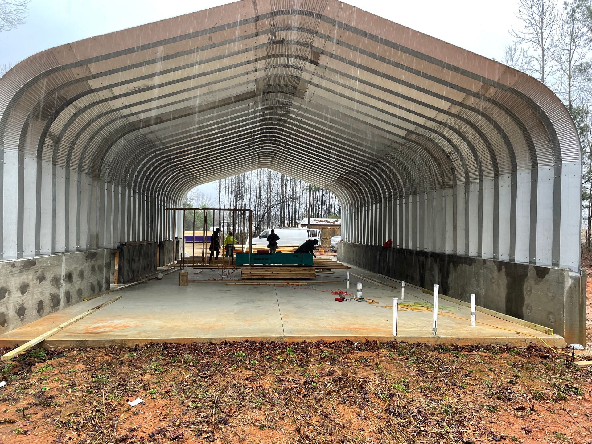 Covered metal shed with a concrete floor under construction, seen from the open entrance.