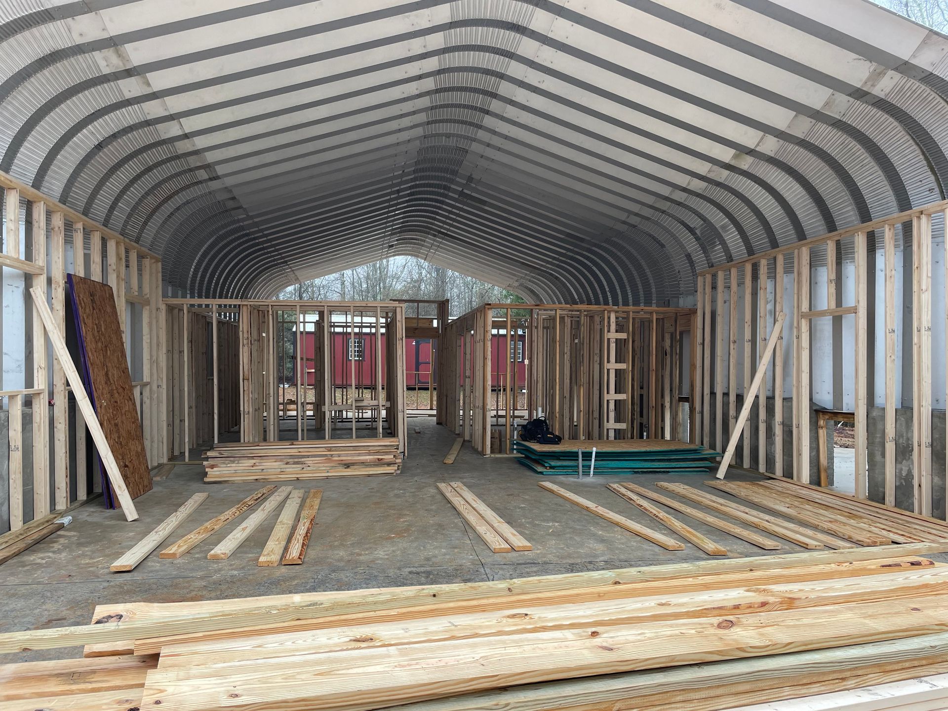 Interior of a wooden-framed building under construction with arched roof framing and lumber stacked on the floor