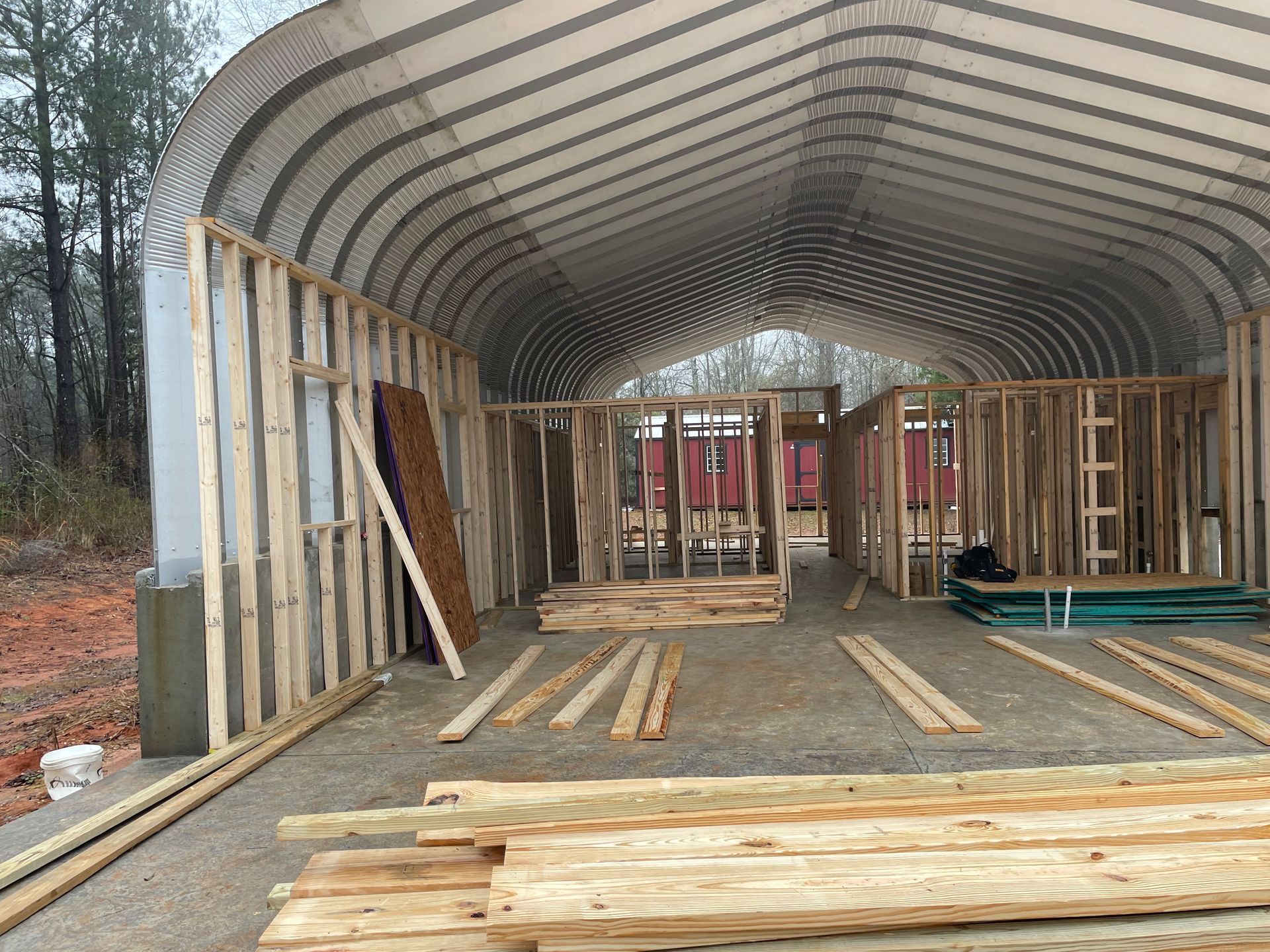 Framed wooden structure under a large curved metal roof at a construction site