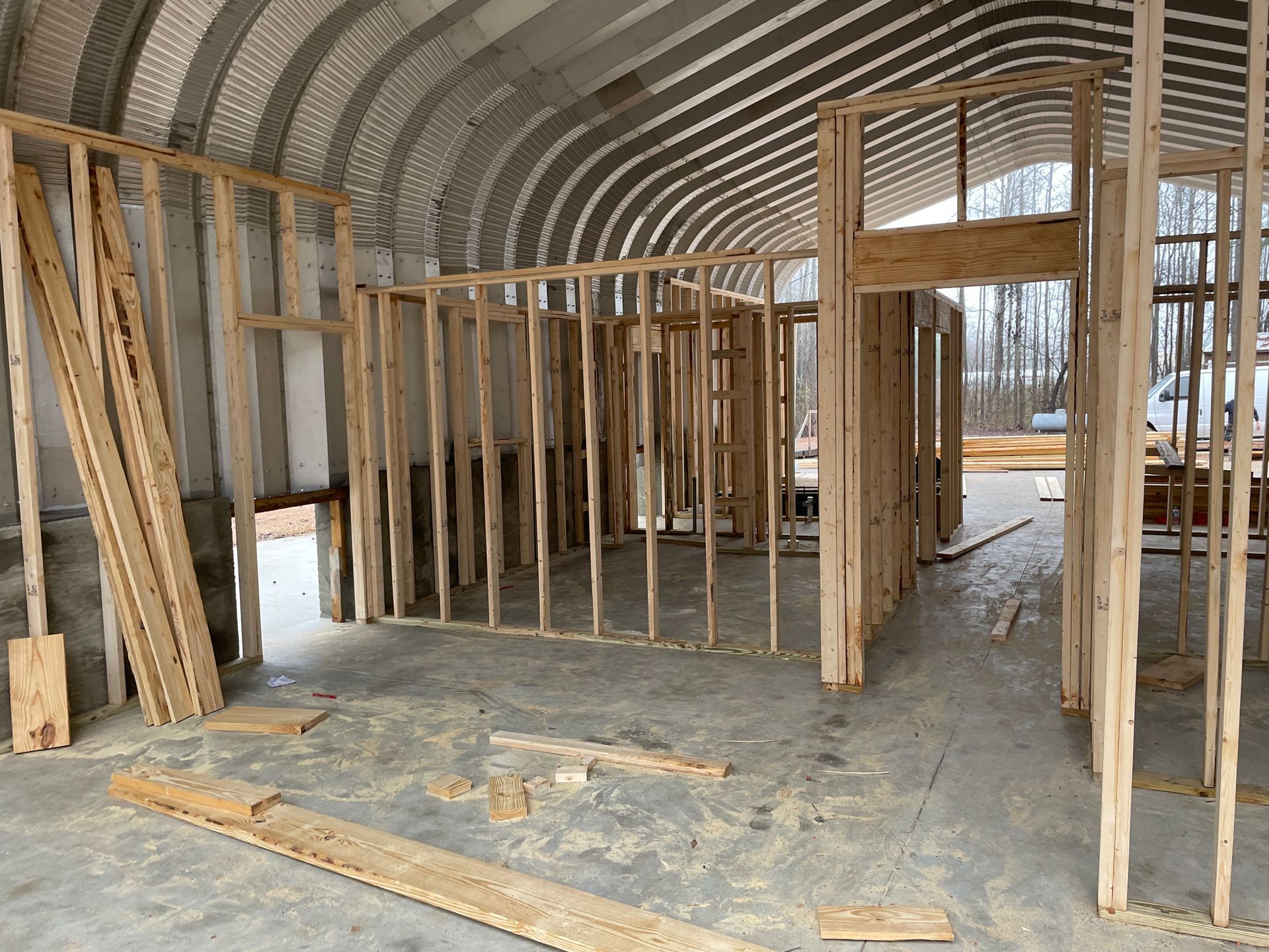 Interior of an unfinished arched metal building with wood framing and a concrete floor under construction