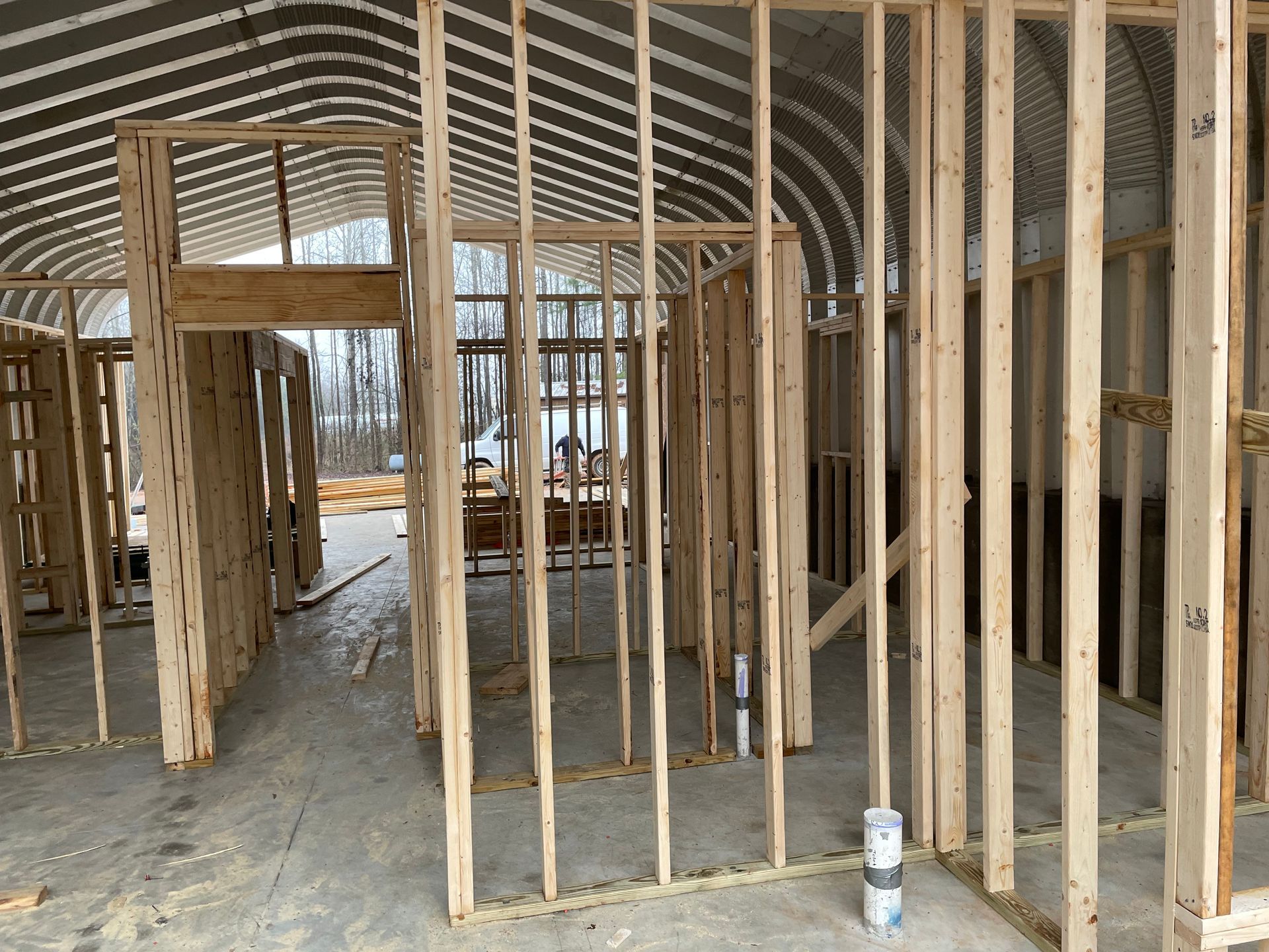 Unfinished house framing with exposed wooden studs and arched roof trusses inside a construction site.