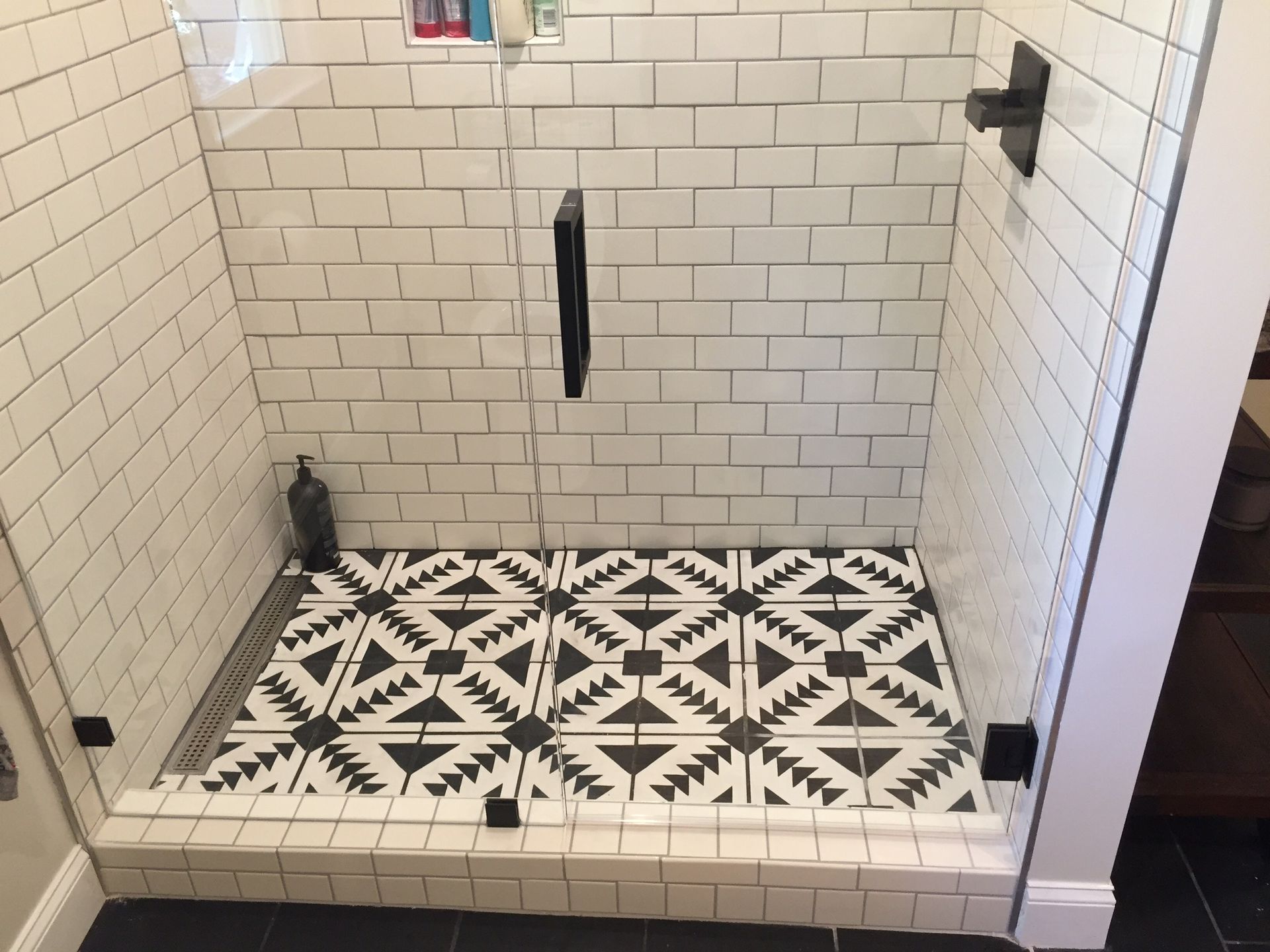 Empty tiled shower stall with black-and-white patterned floor and white subway walls