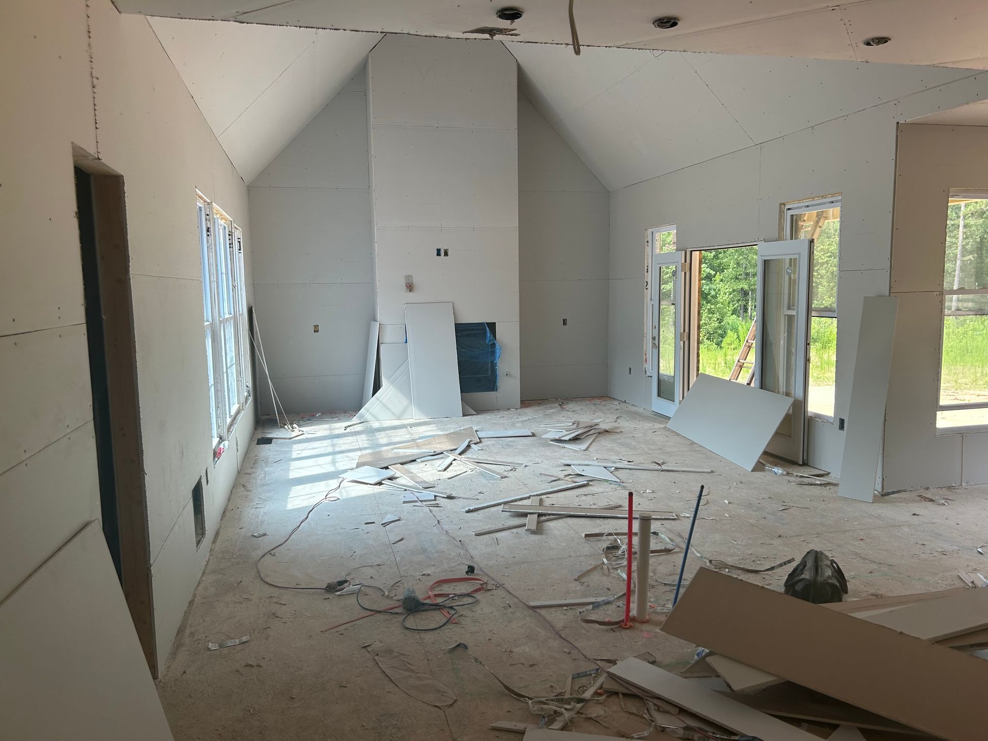 Damaged room under renovation with debris on the floor, exposed ceiling, and unfinished walls by windows