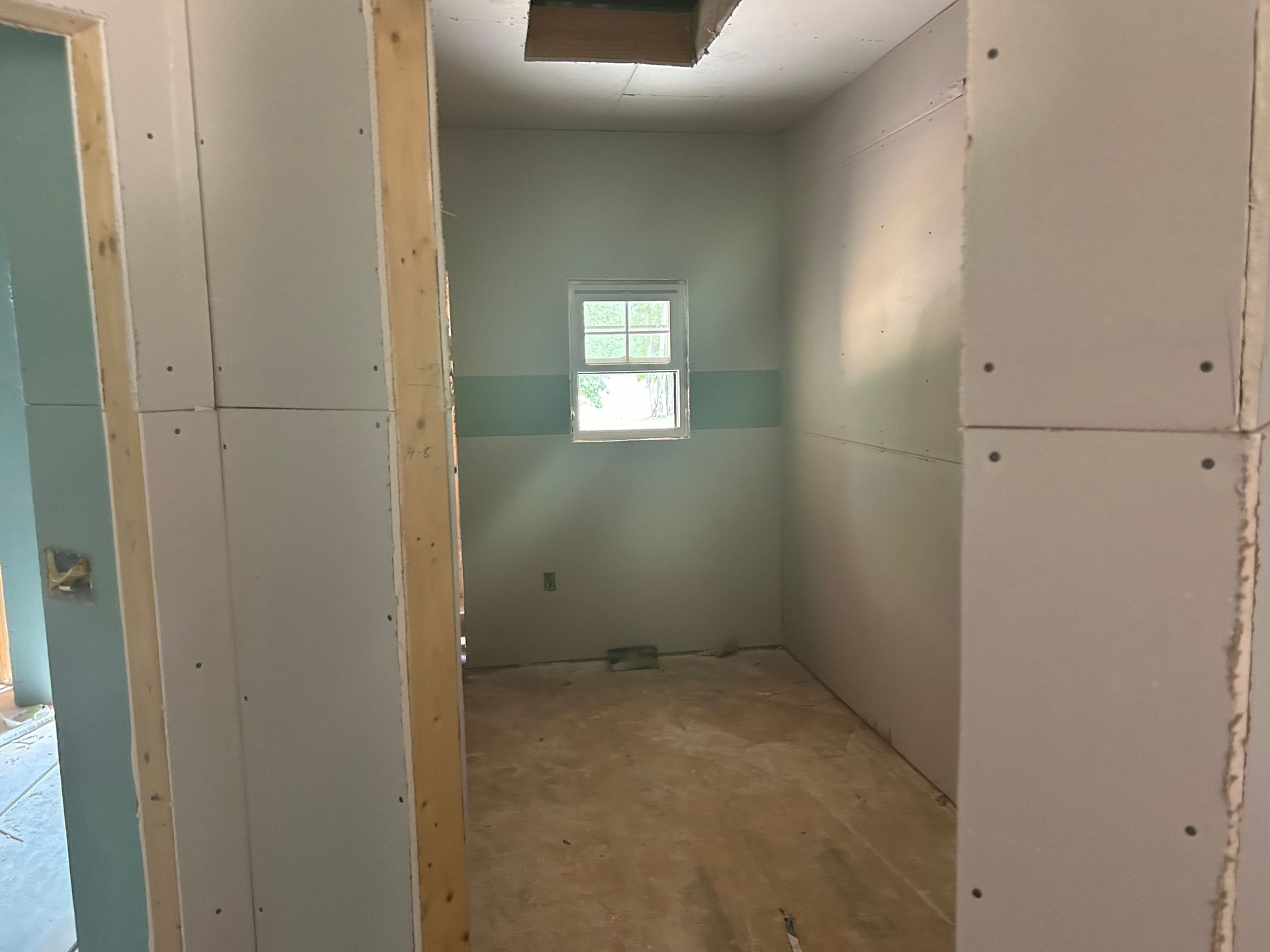 Narrow unfinished room with drywall walls, a small window, and exposed ceiling opening.