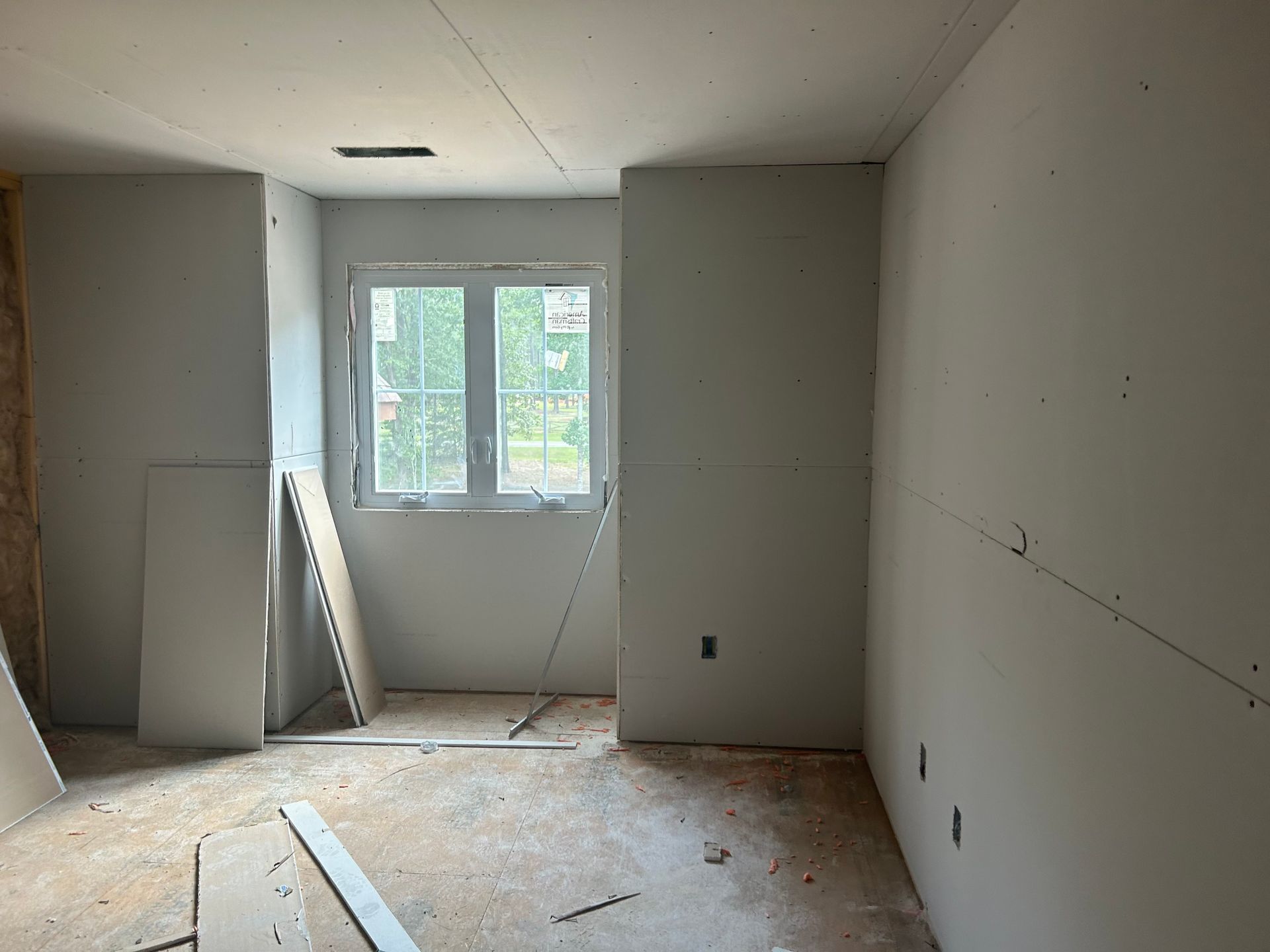 Unfinished room with bare walls, window, and construction debris on the floor.
