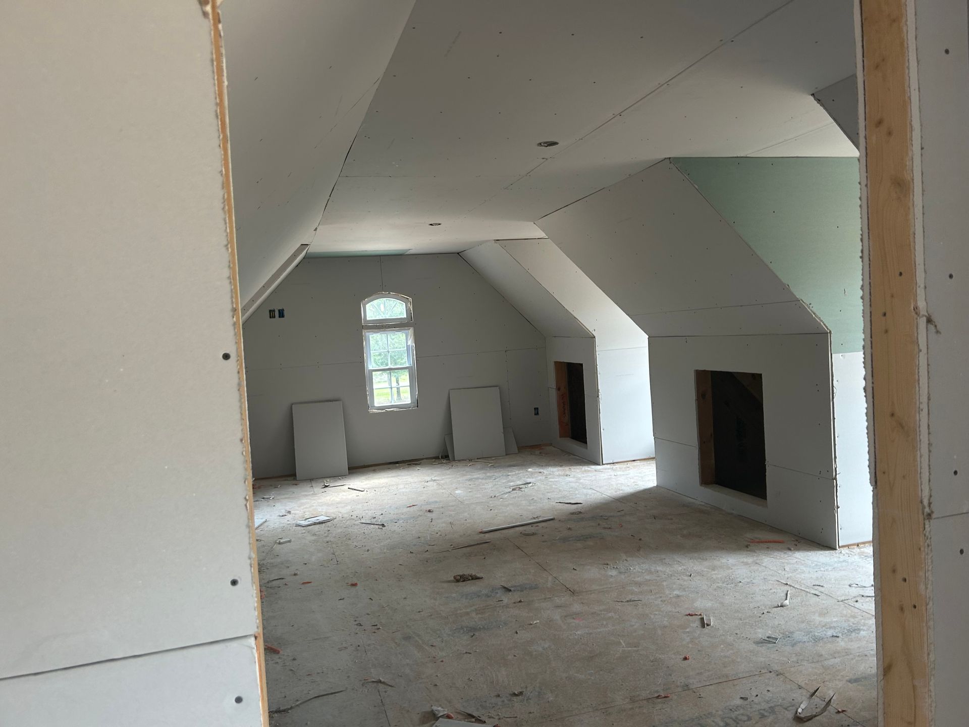 Empty unfinished attic room with sloped white walls, exposed fireplace, and small window.