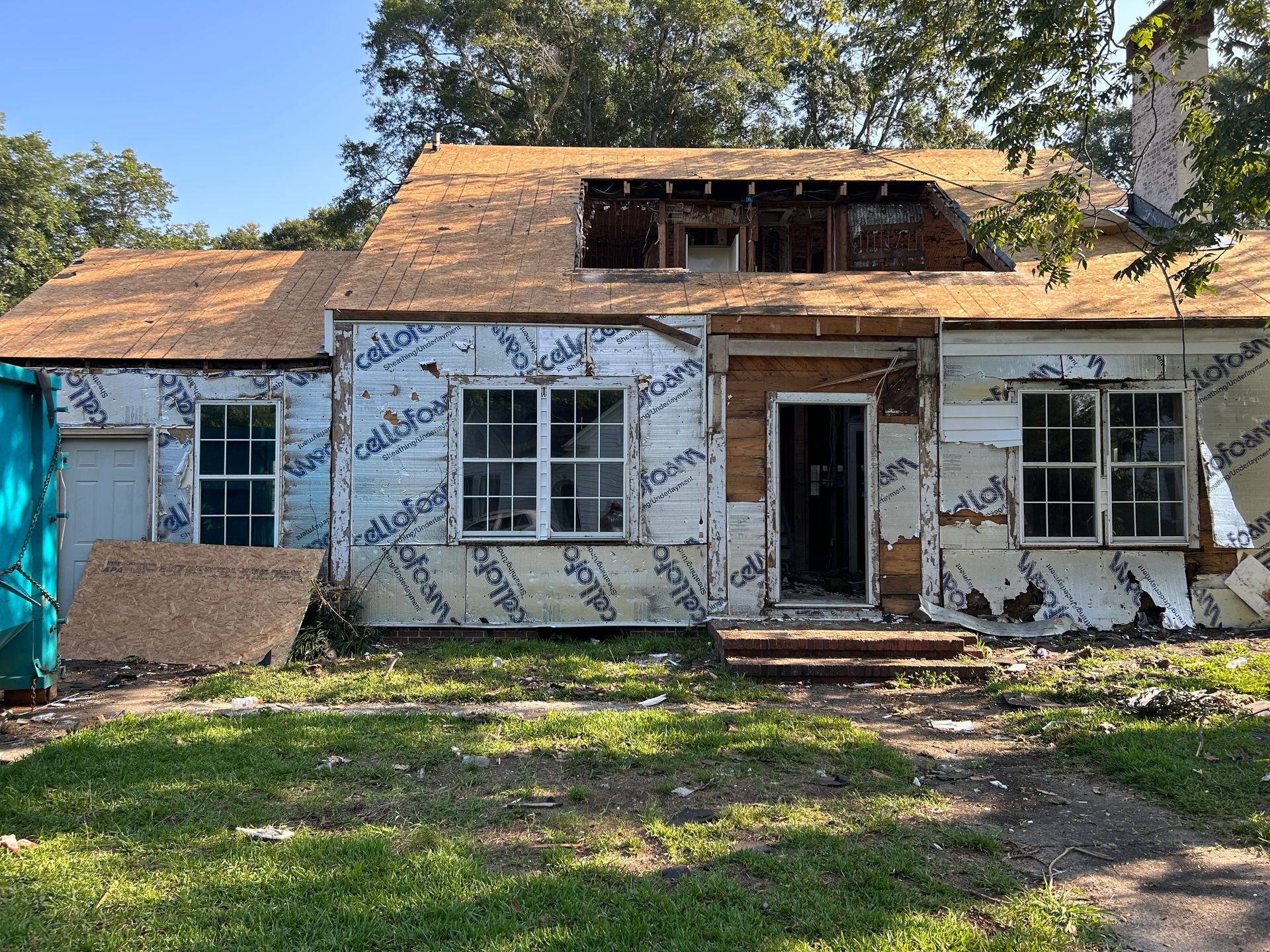Abandoned, weathered house with boarded windows and peeling exterior paint, surrounded by trees and grass.