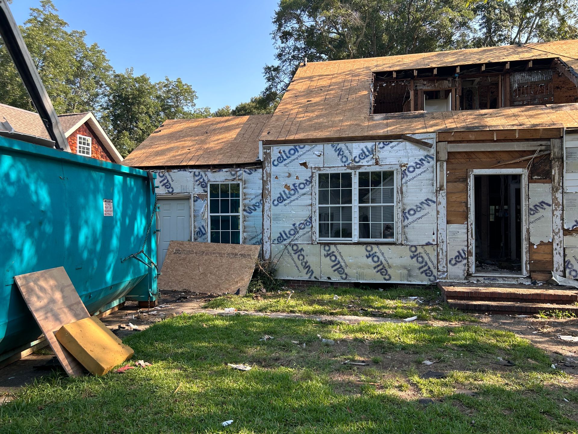 Partially demolished house with exposed framing, blue tarp wall, and construction debris in the yard