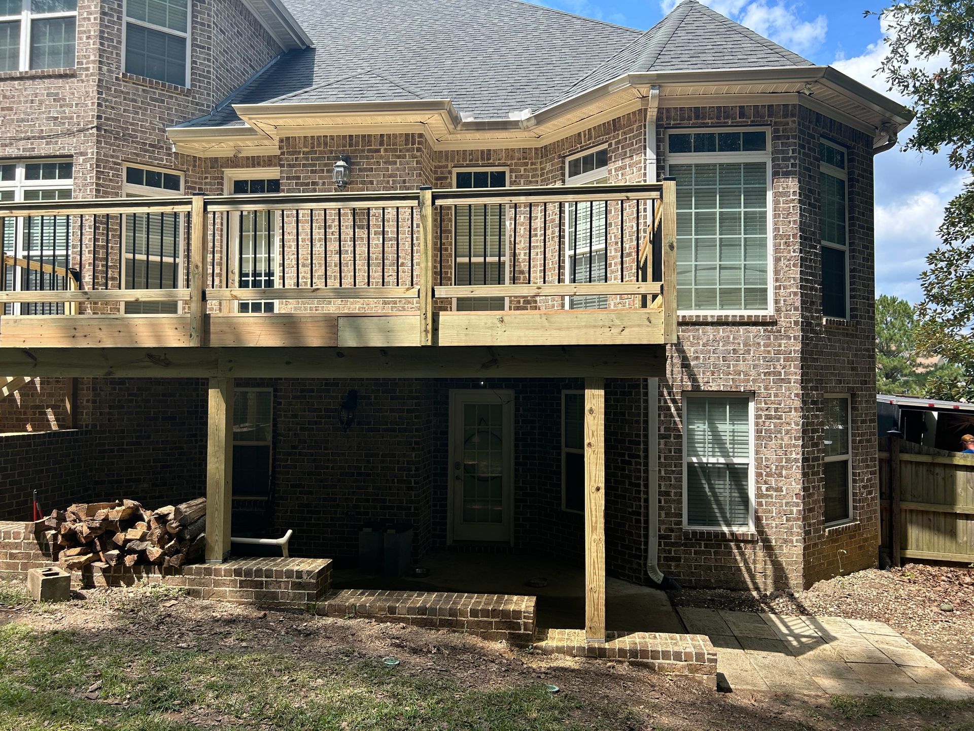 Brick house with a wooden deck and covered patio, viewed from the backyard.