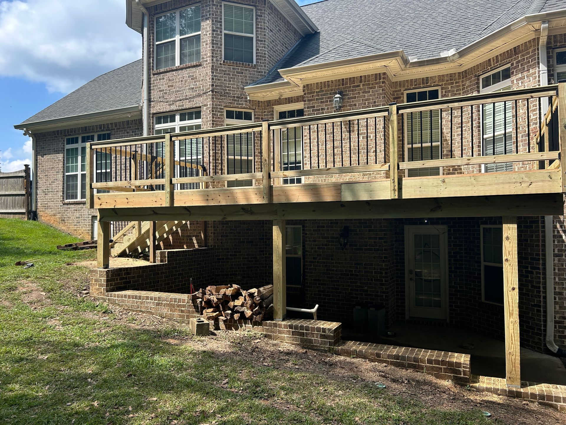 Raised wooden deck on a brick house with railing, stairs, and a shaded patio underneath.