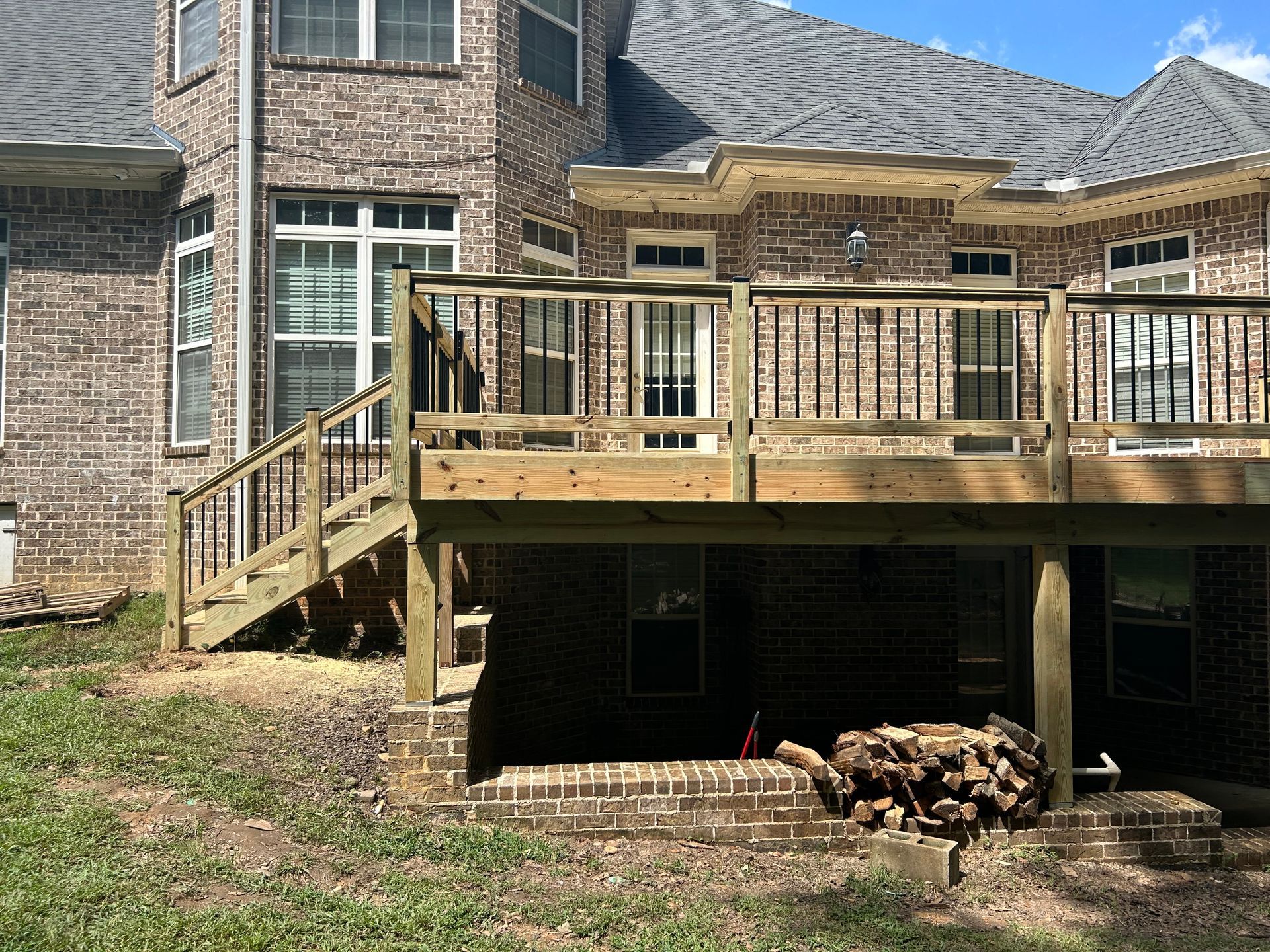 Wooden deck on the back of a brick house with stairs leading to a shaded basement area.