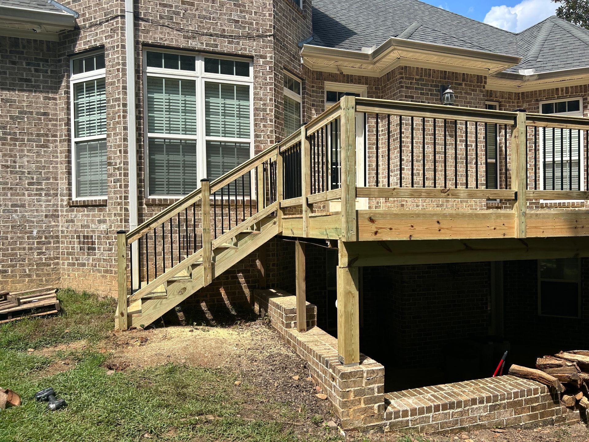 Brick house exterior with wooden deck, stairs, and a raised patio over a shaded basement area