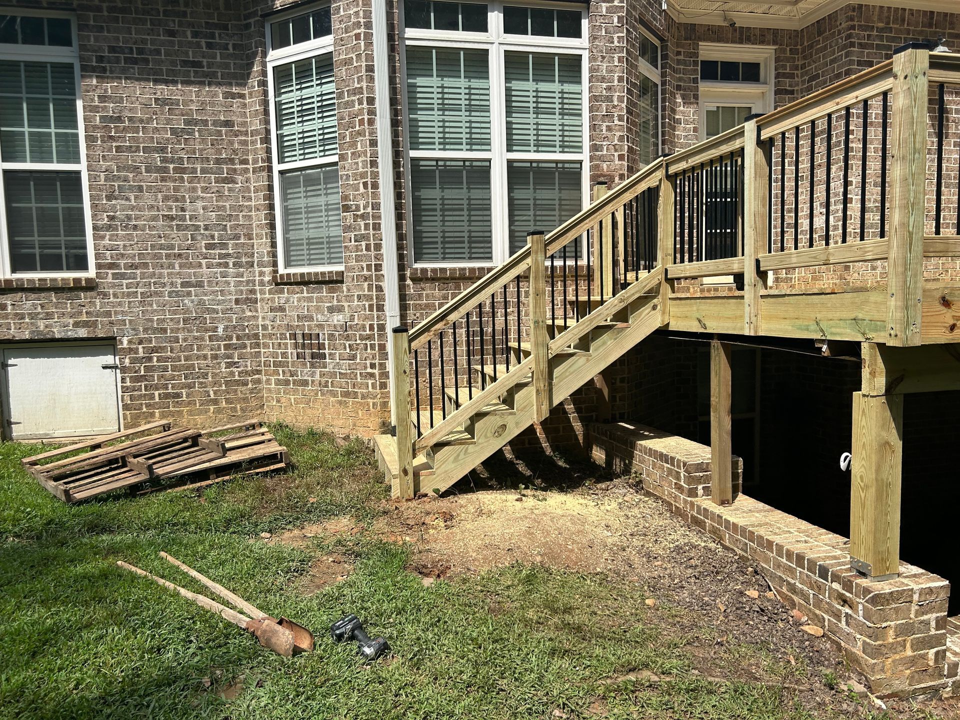 Brick house patio with wooden stairs, grassy yard, and a rake on the ground