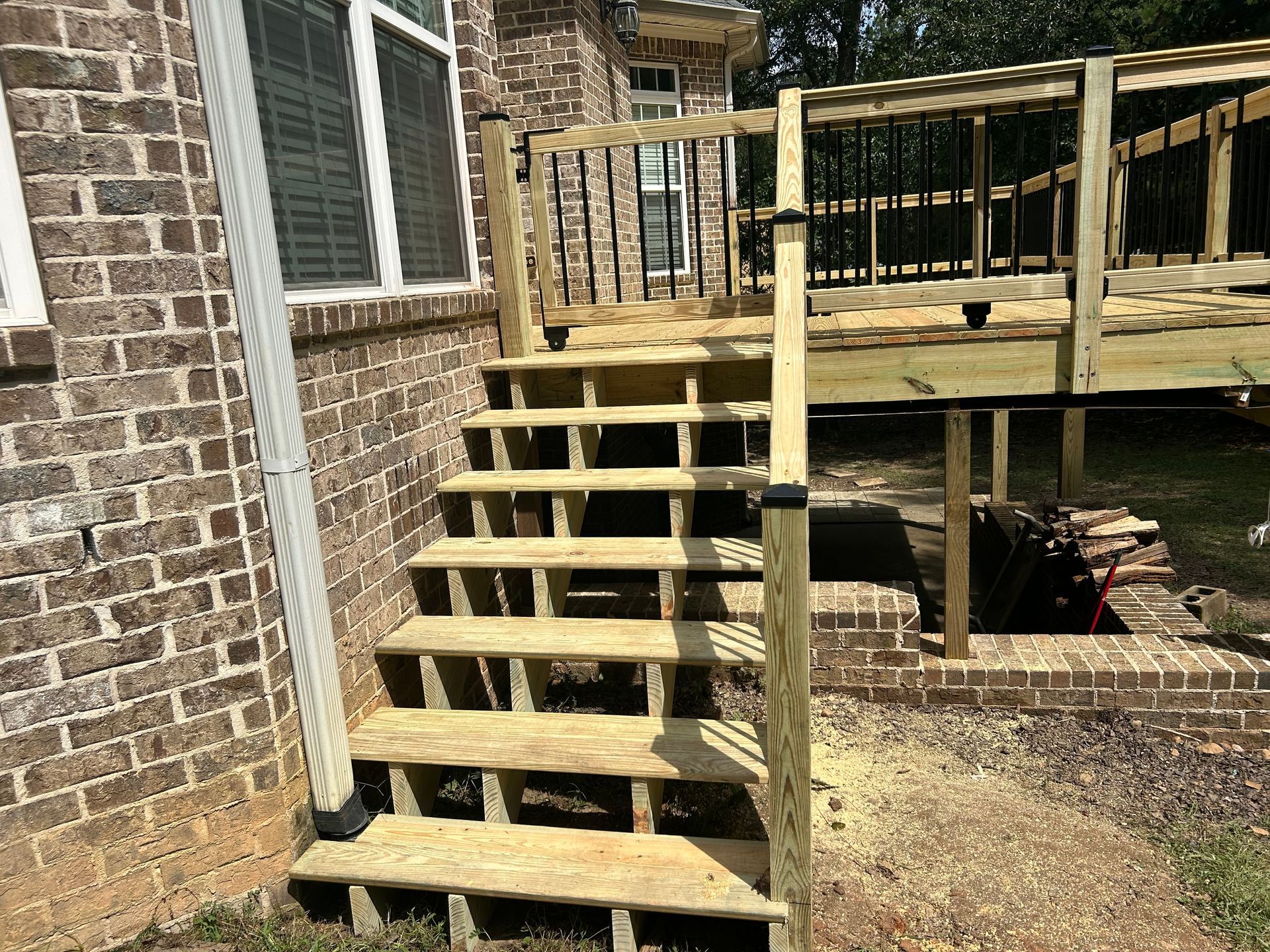 Wooden outdoor stairs leading to a raised deck beside a brick house