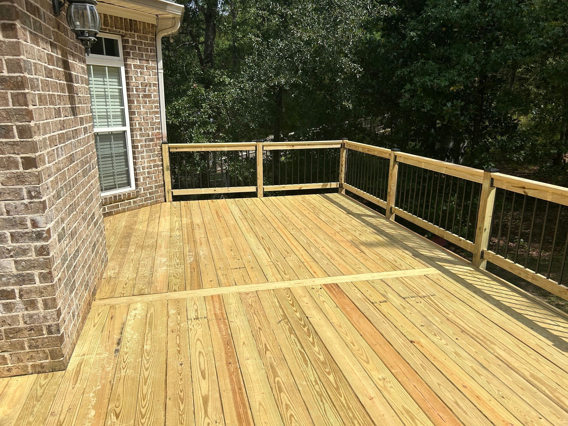 New wooden deck beside a brick house, with railing and wooded backyard.