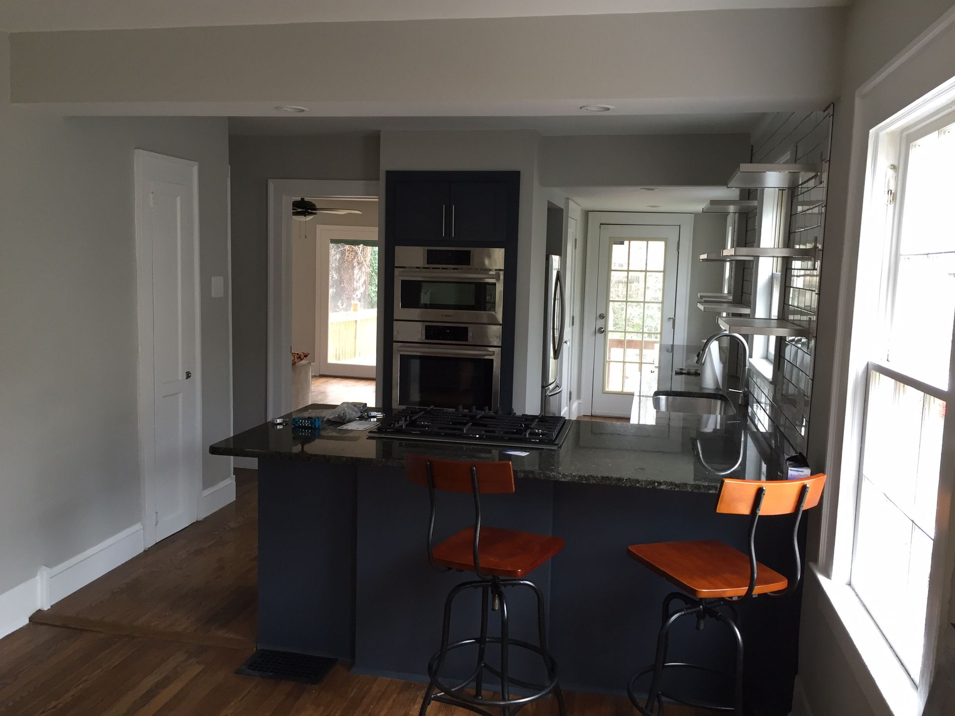 Modern kitchen with dark island, orange bar stools, hardwood floors, and bright glass doors.