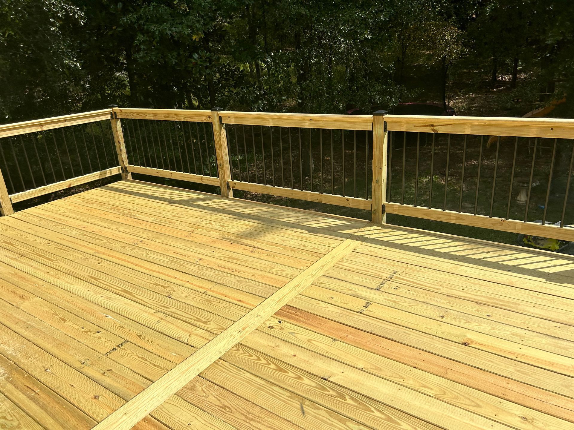 Wooden deck with railing overlooking a wooded area in bright sunlight