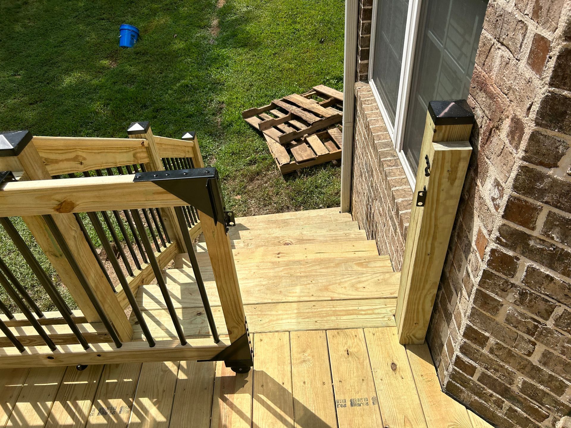 Wooden backyard stairs and deck leading to a grassy yard beside a brick house.