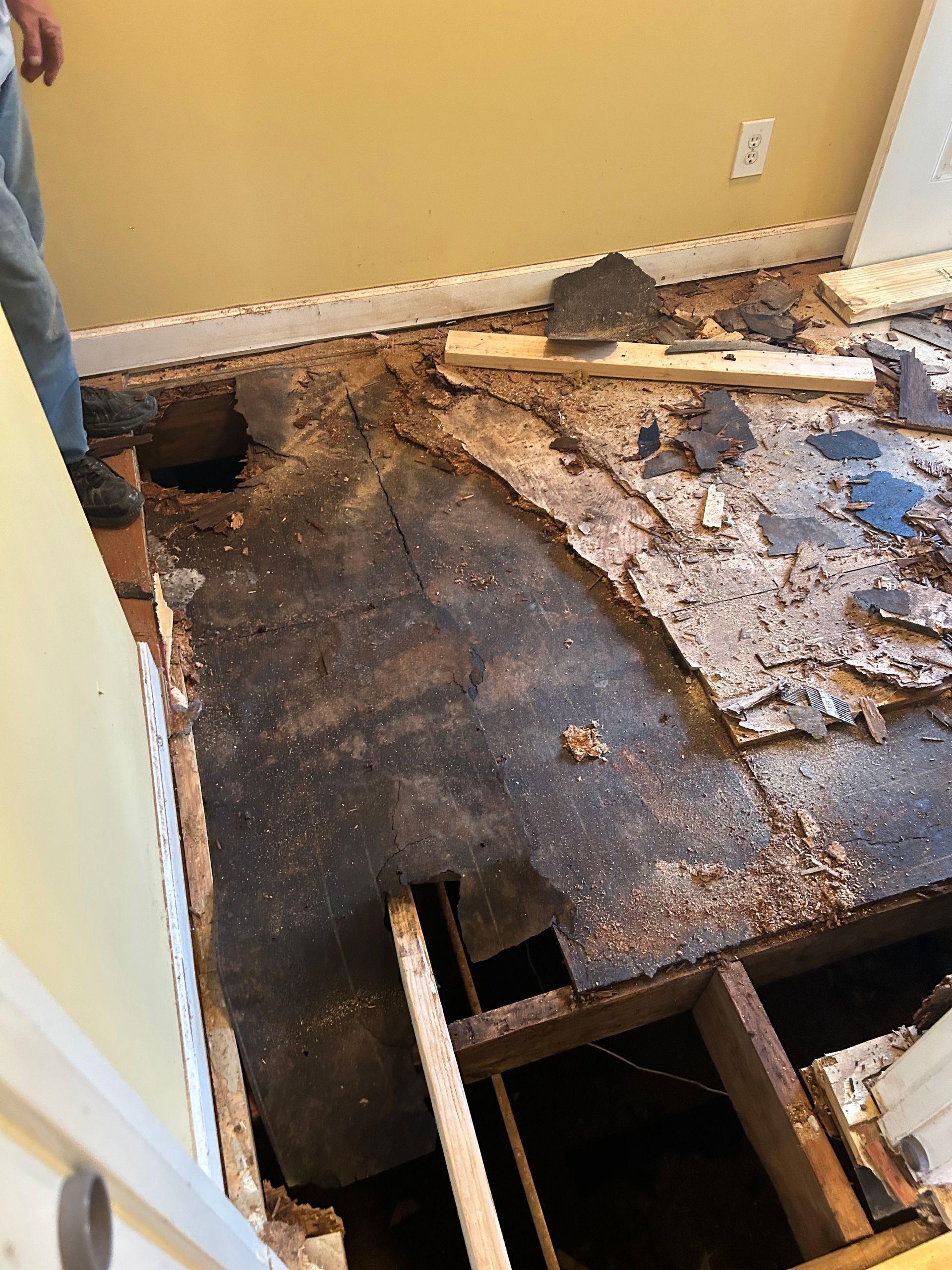 Damaged floor with exposed joists and torn flooring in a room corner