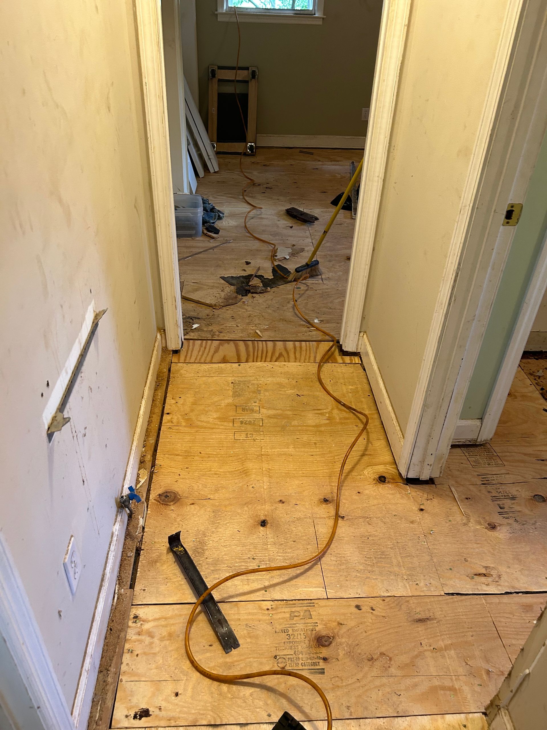 Hallway with damaged flooring, debris, and a loose cable across the floor ahead.
