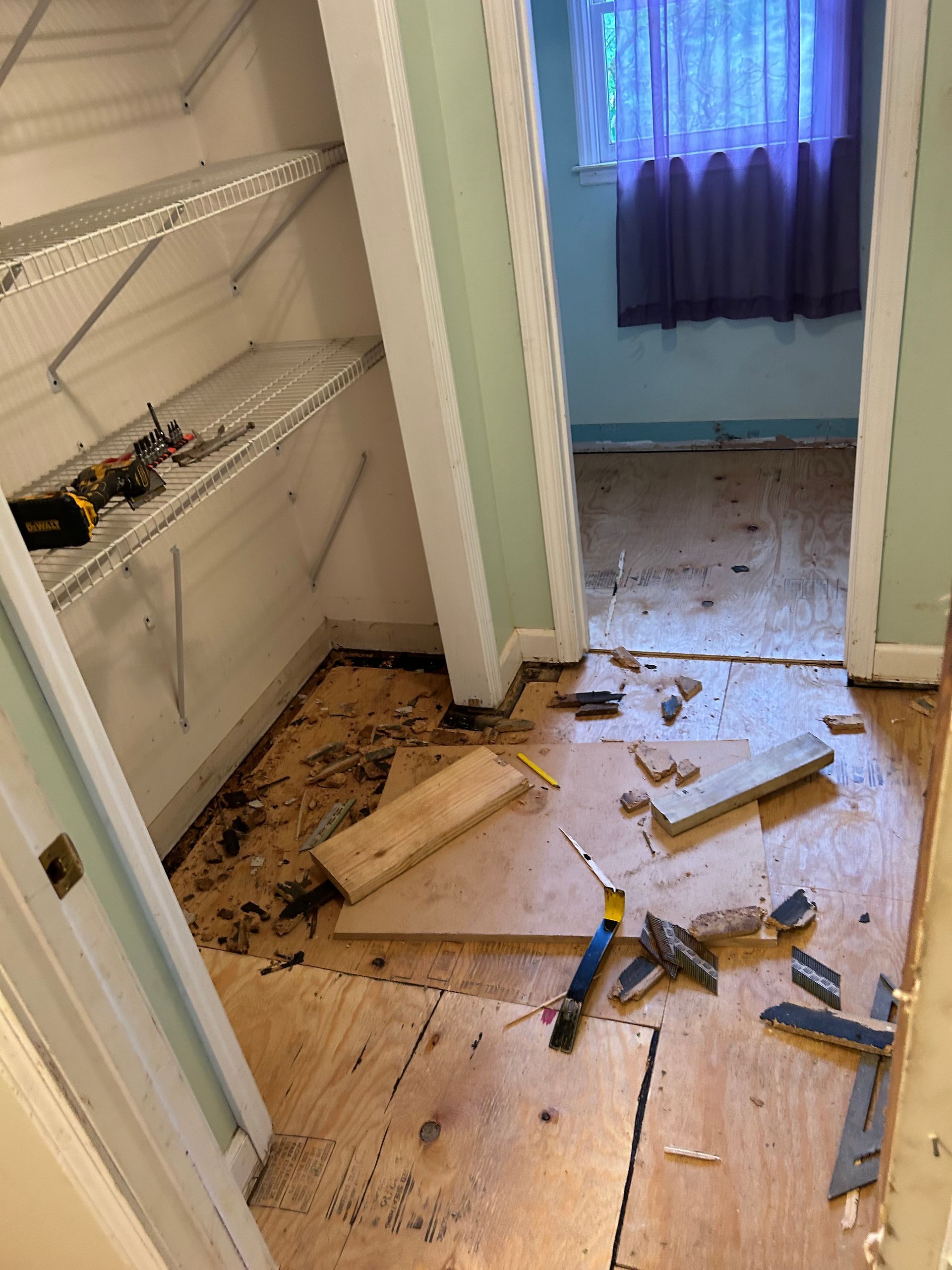 Damaged hallway and closet with broken floorboards, debris, and tools on the floor