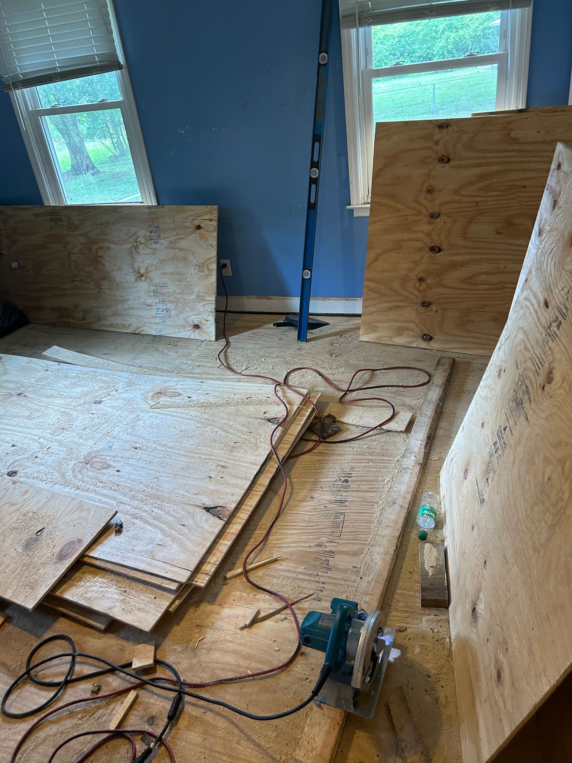 Plywood barriers and cords in a blue-walled room with windows, suggesting a construction or renovation site