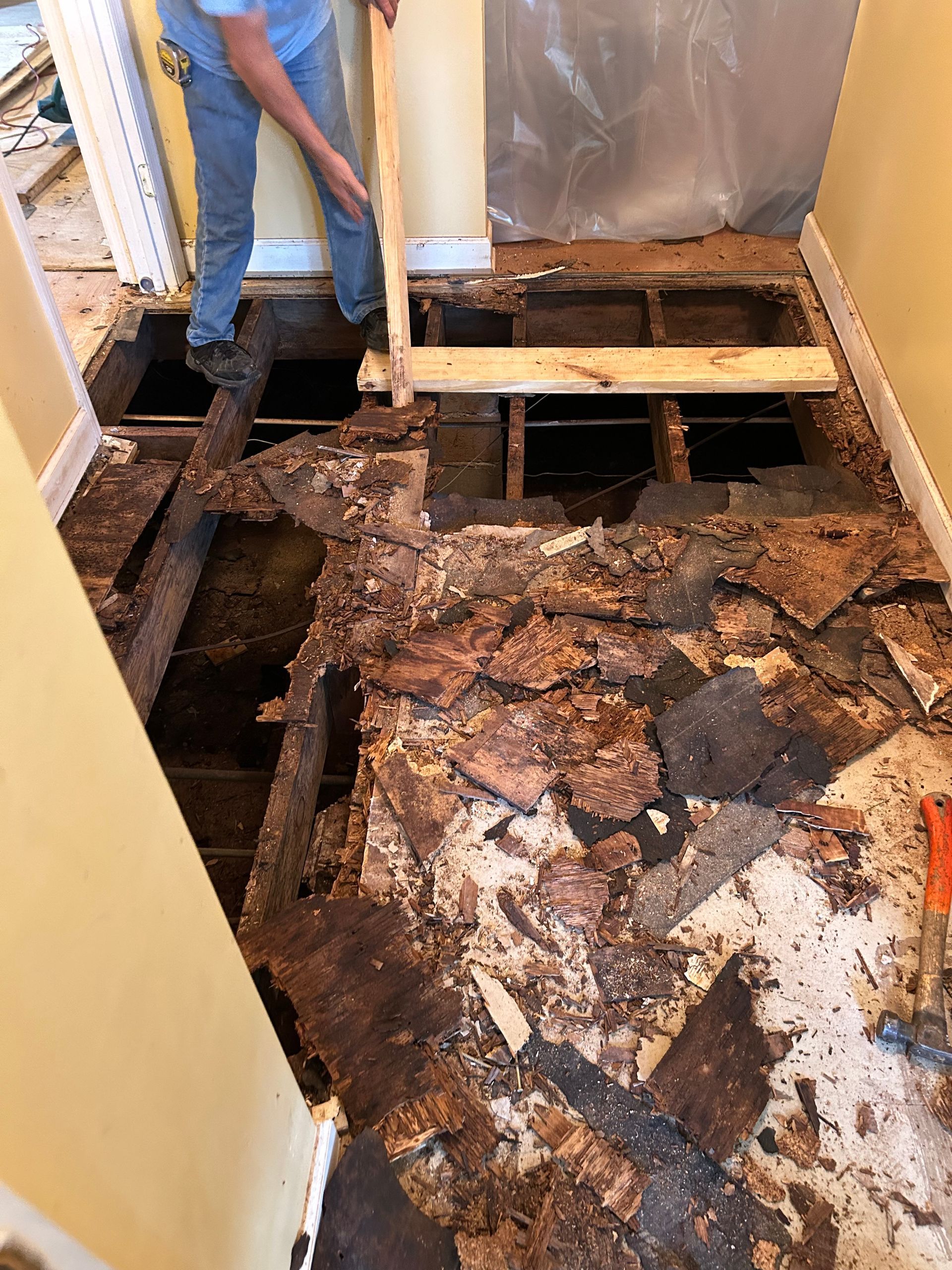 Rusted, water-damaged floor boards in a room, with a person standing near an open floor section.