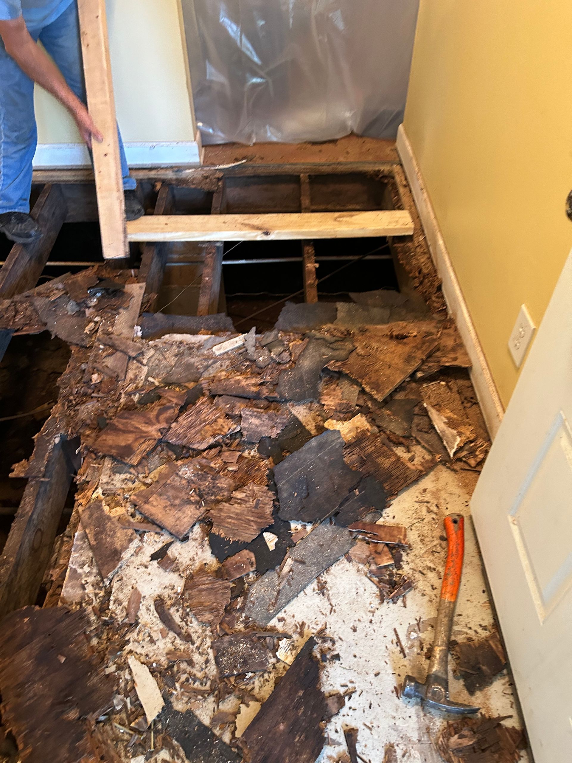 Damaged bathroom floor with exposed subfloor, broken tiles, and debris during renovation