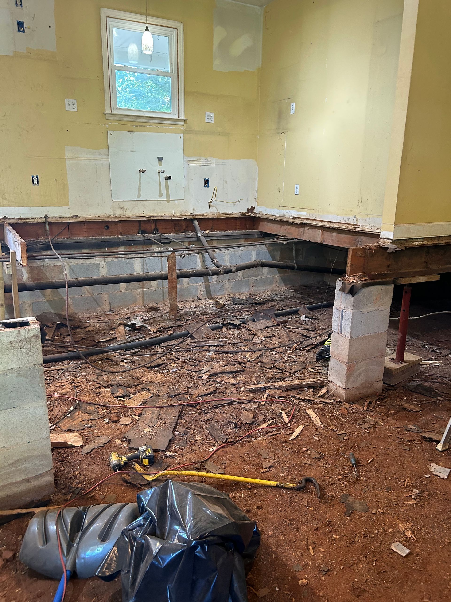Kitchen under renovation with exposed floor joists, debris, and partially removed cabinets.