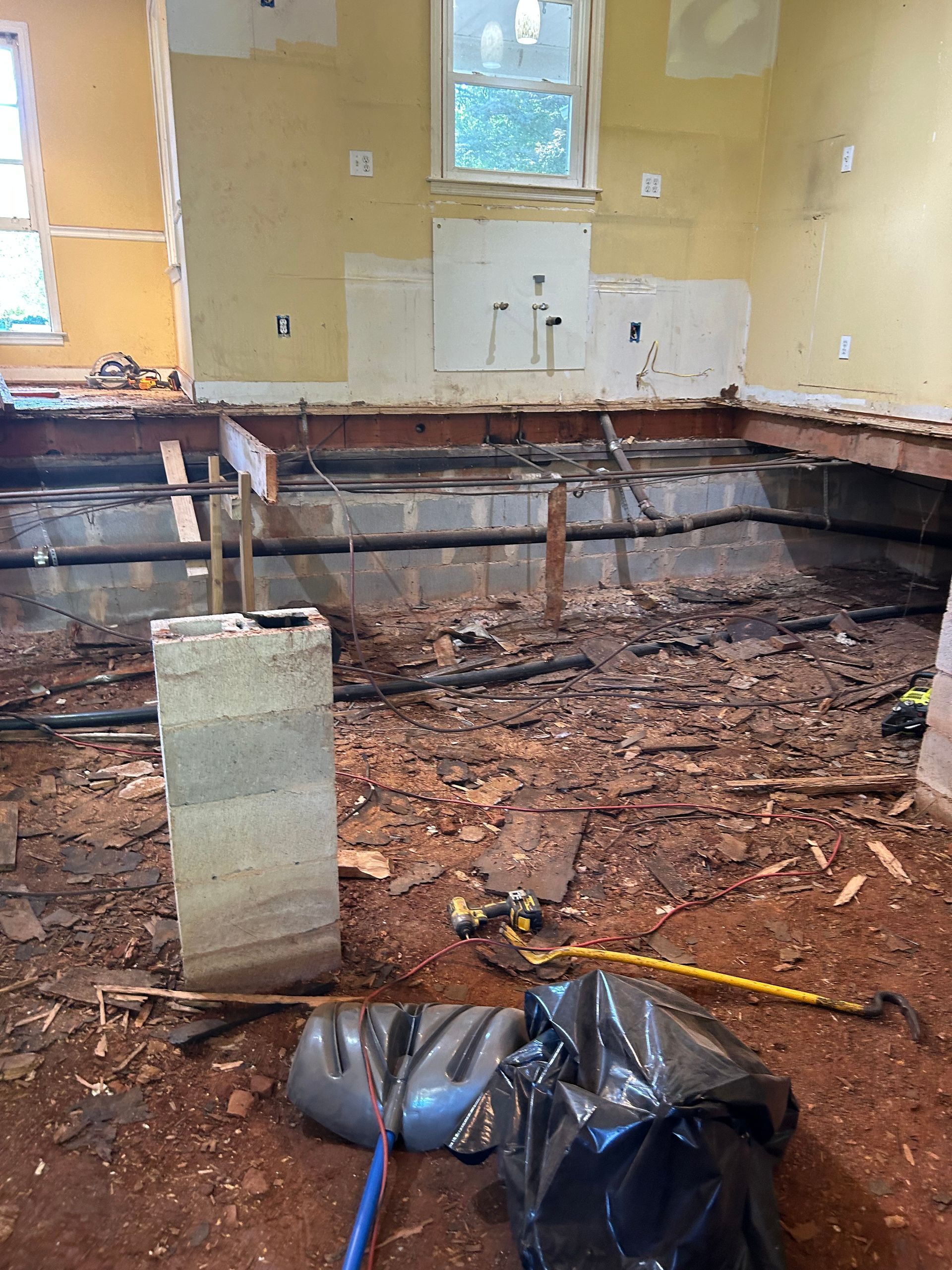 Interior room under renovation with exposed floor joists, debris, and tools on the floor