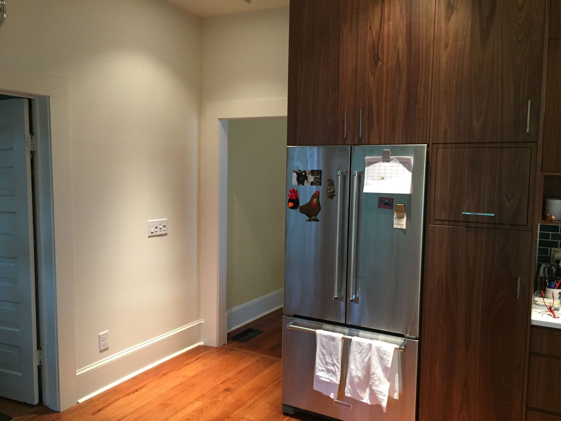 Kitchen corner with stainless fridge, wooden cabinets, and sunlight on hardwood floor.