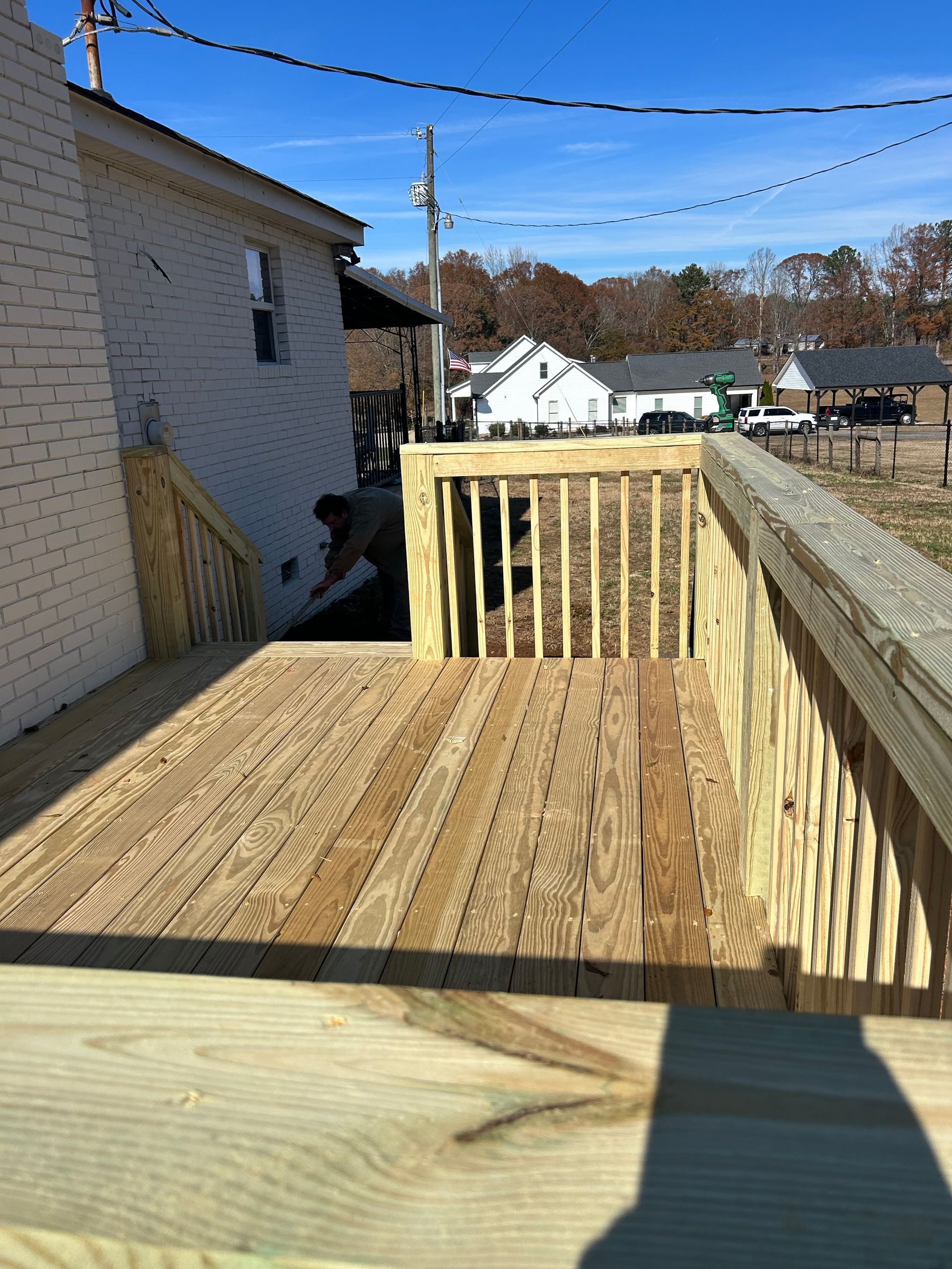 Wooden deck under construction beside a house, with railings and a sunny residential backyard.