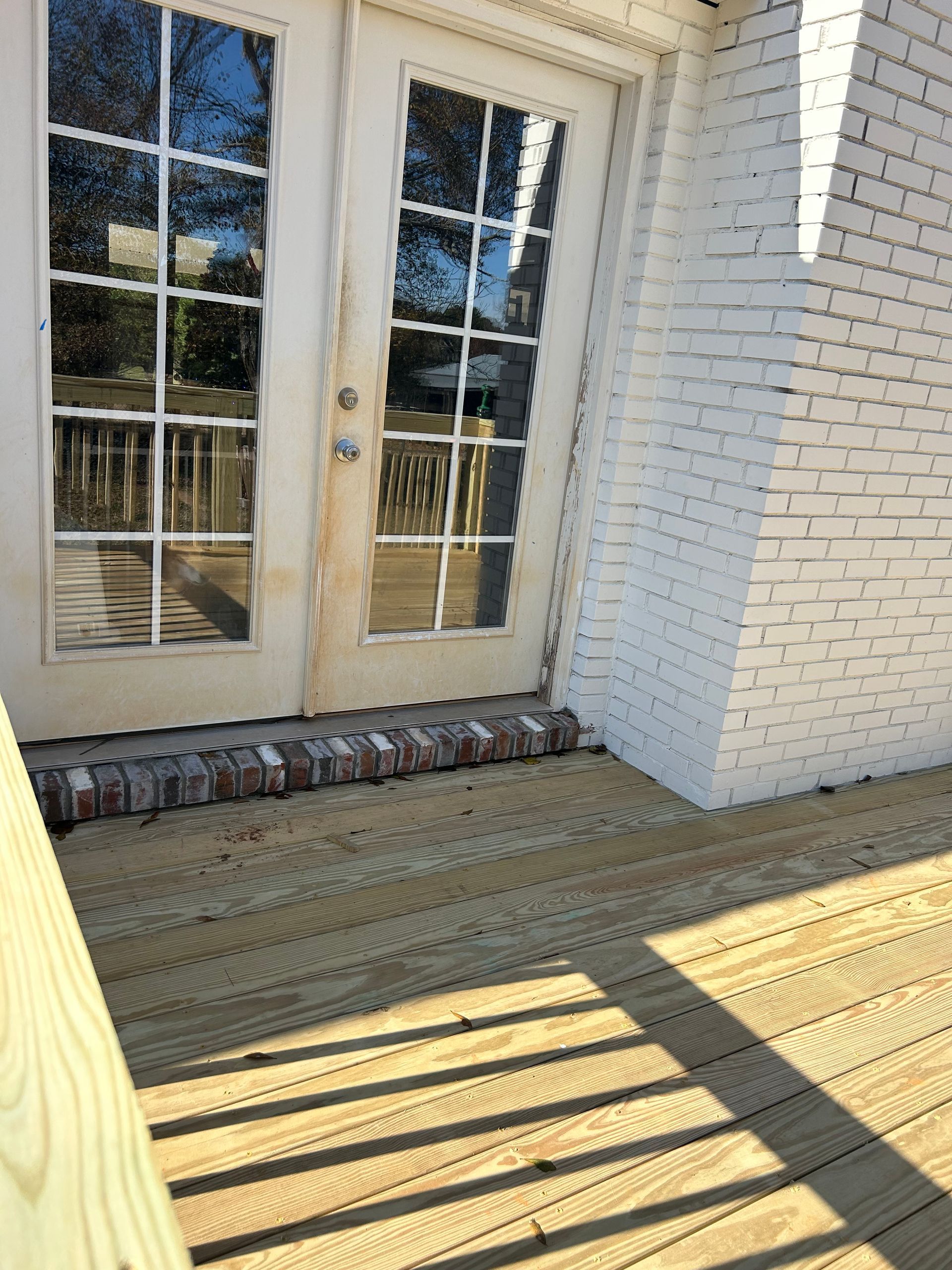 White brick porch with glass French doors and sunlit wooden steps leading to a deck
