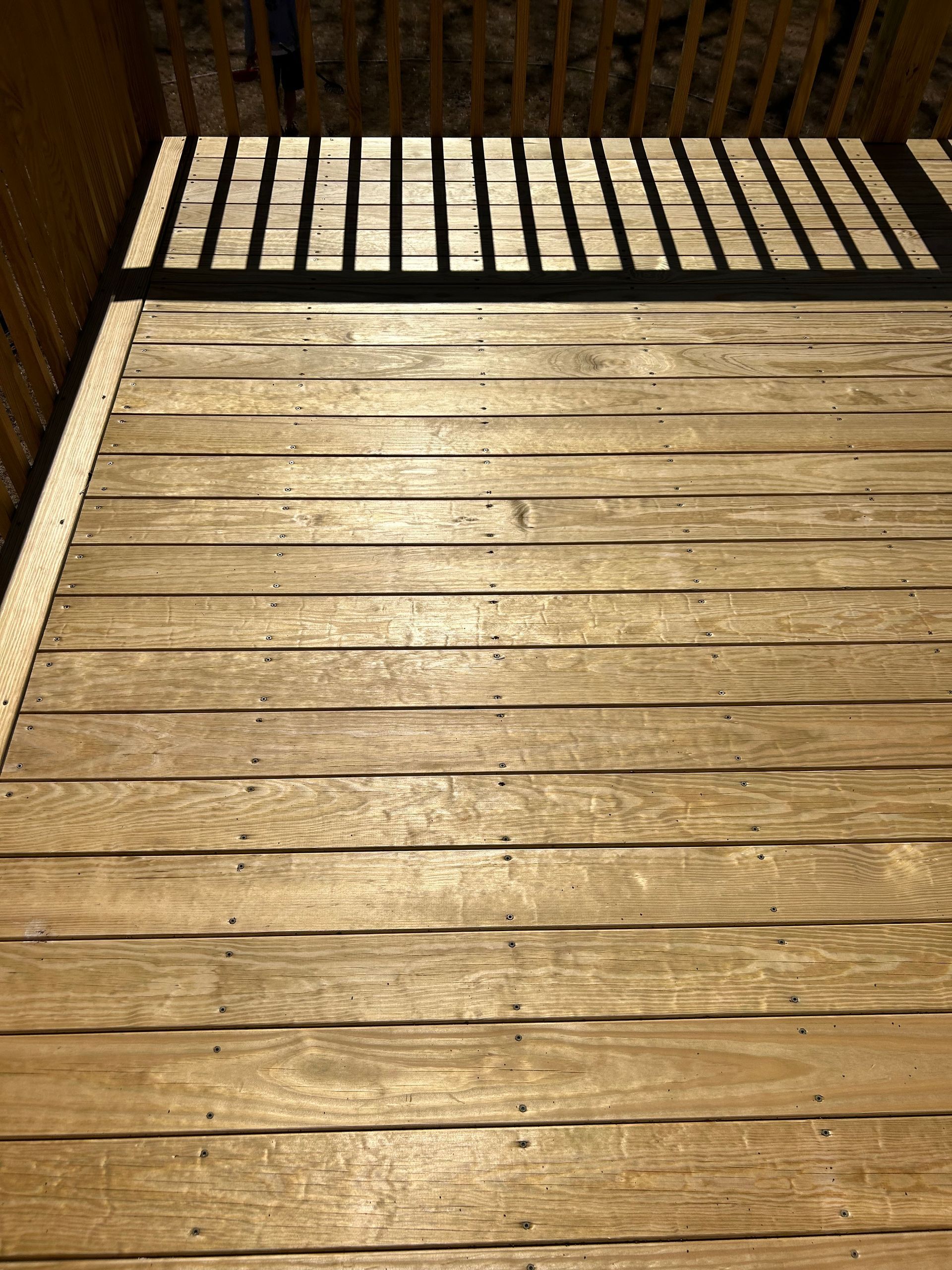 Wooden deck with a white railing casting shadows in bright sunlight