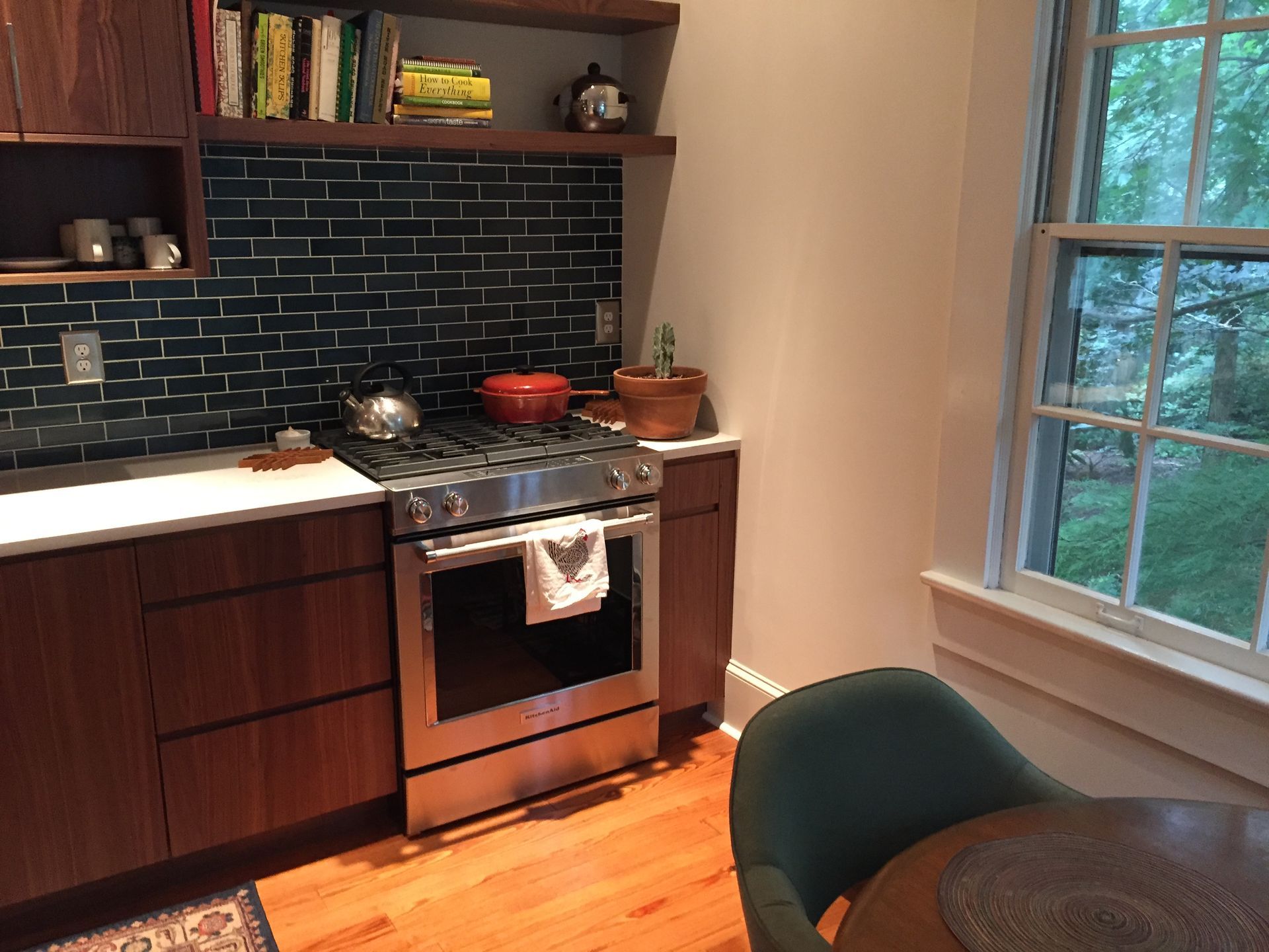 Modern kitchen with dark cabinets, black tile backsplash, stove, sink, and window beside a small table.
