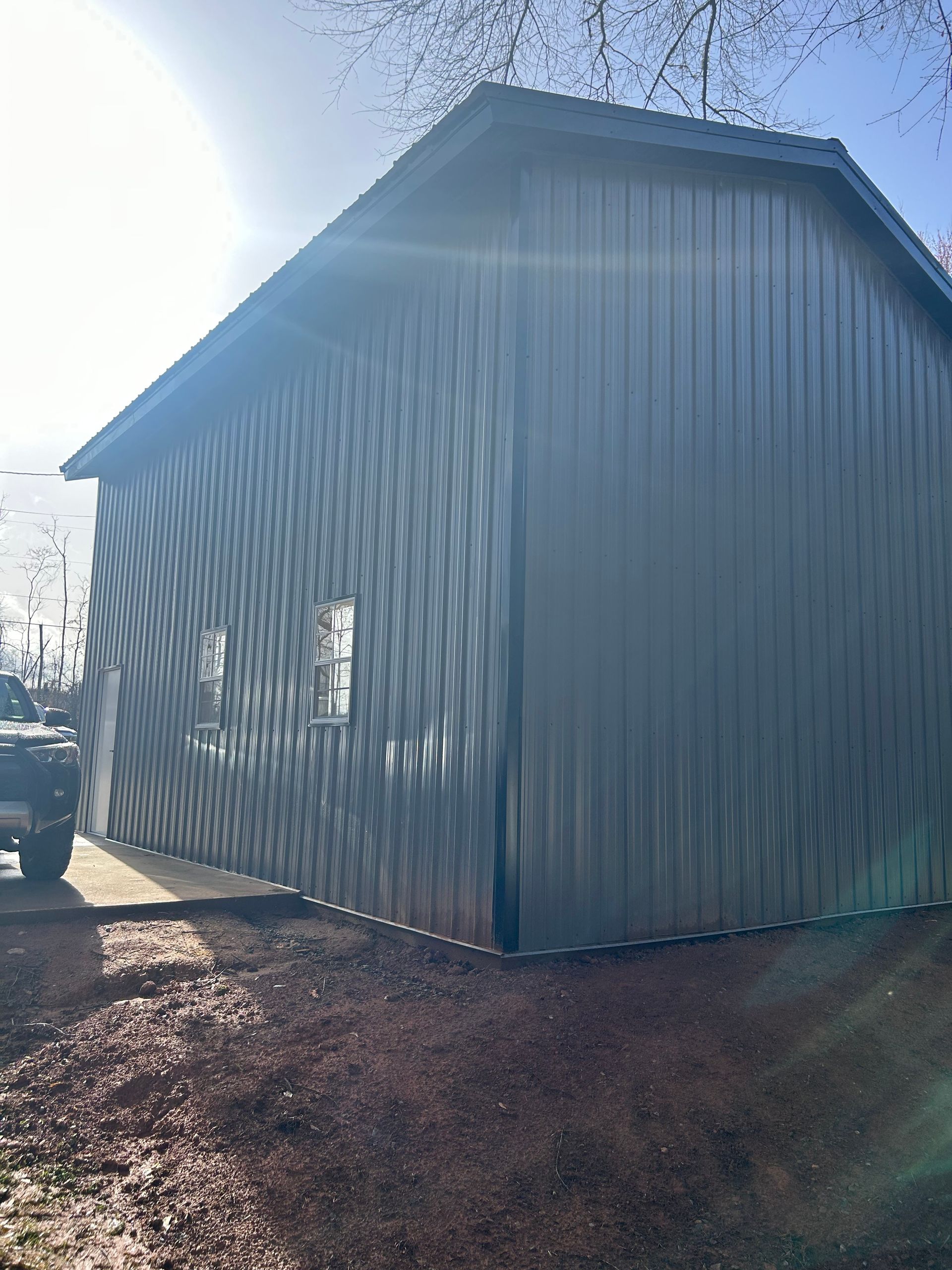 Gray metal-sided barn or shed with a peaked roof in bright sunlight, viewed from the side.