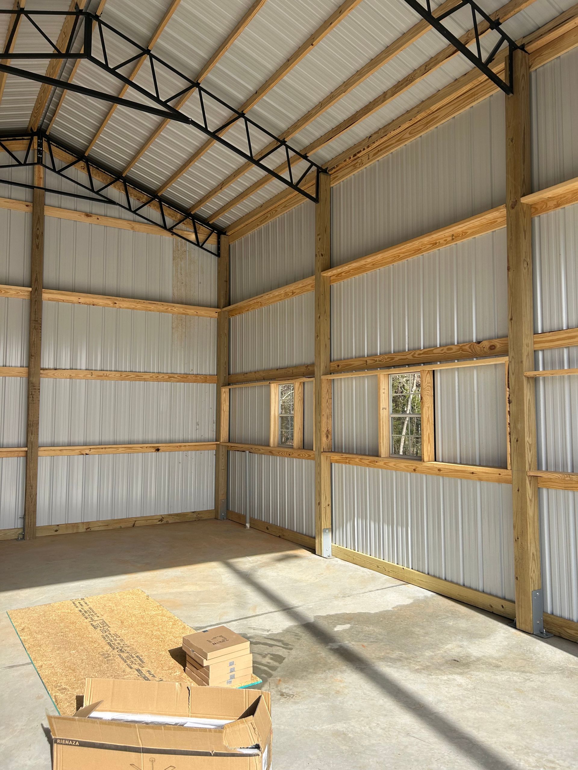 Empty metal-walled shed with exposed roof trusses and sunlight on the concrete floor