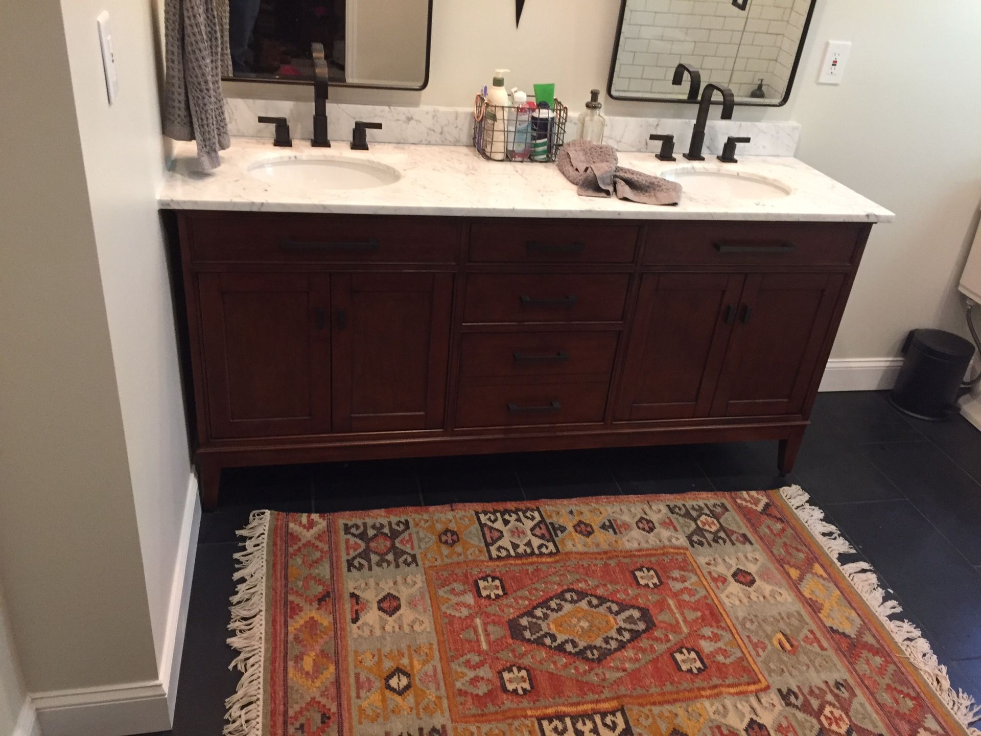 Bathroom vanity with dark wood cabinets, white countertop, mirror, and patterned rug.