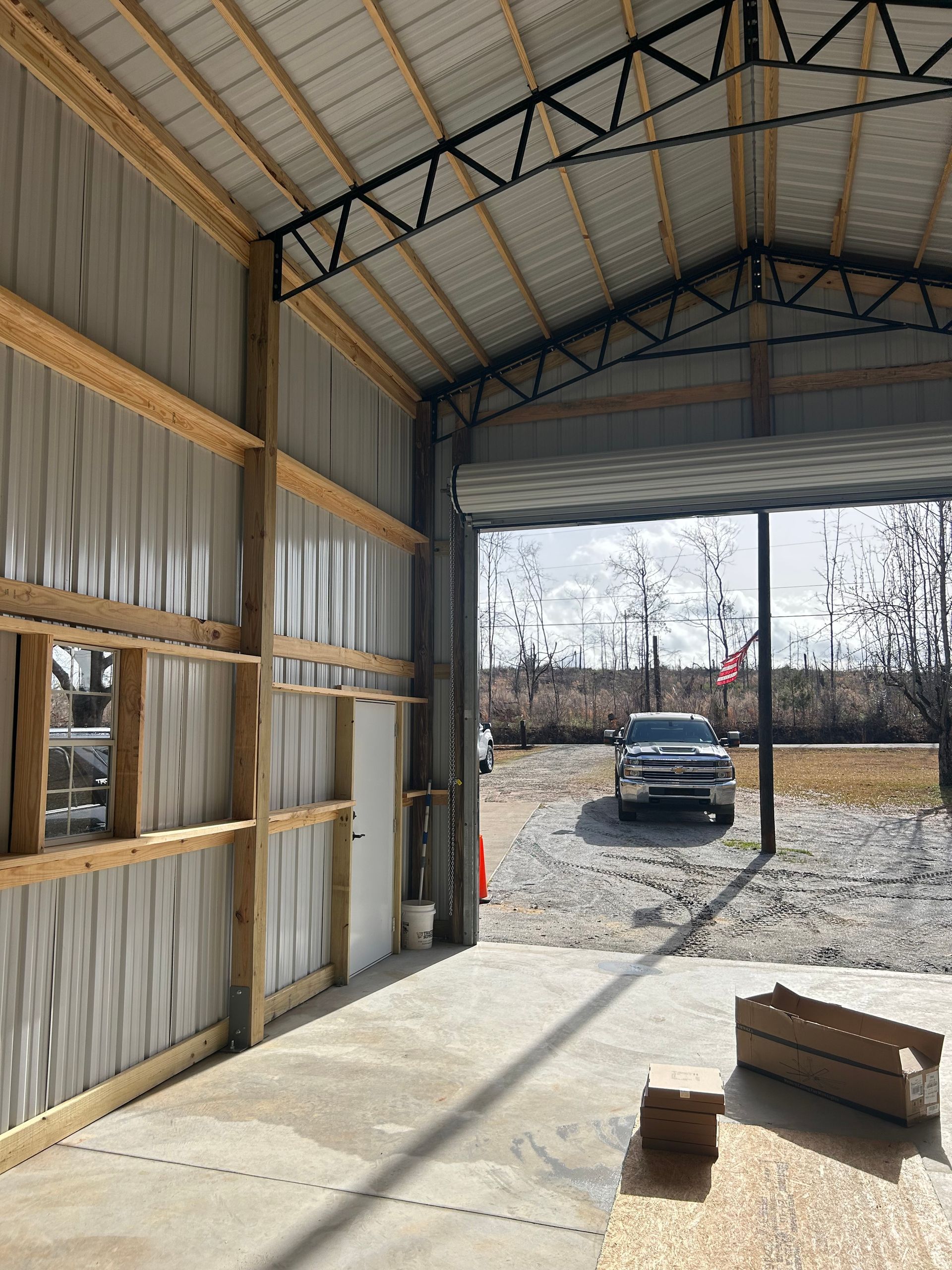 Interior of a metal garage with open door, showing a parked black car outside and sunlight on the concrete floor.