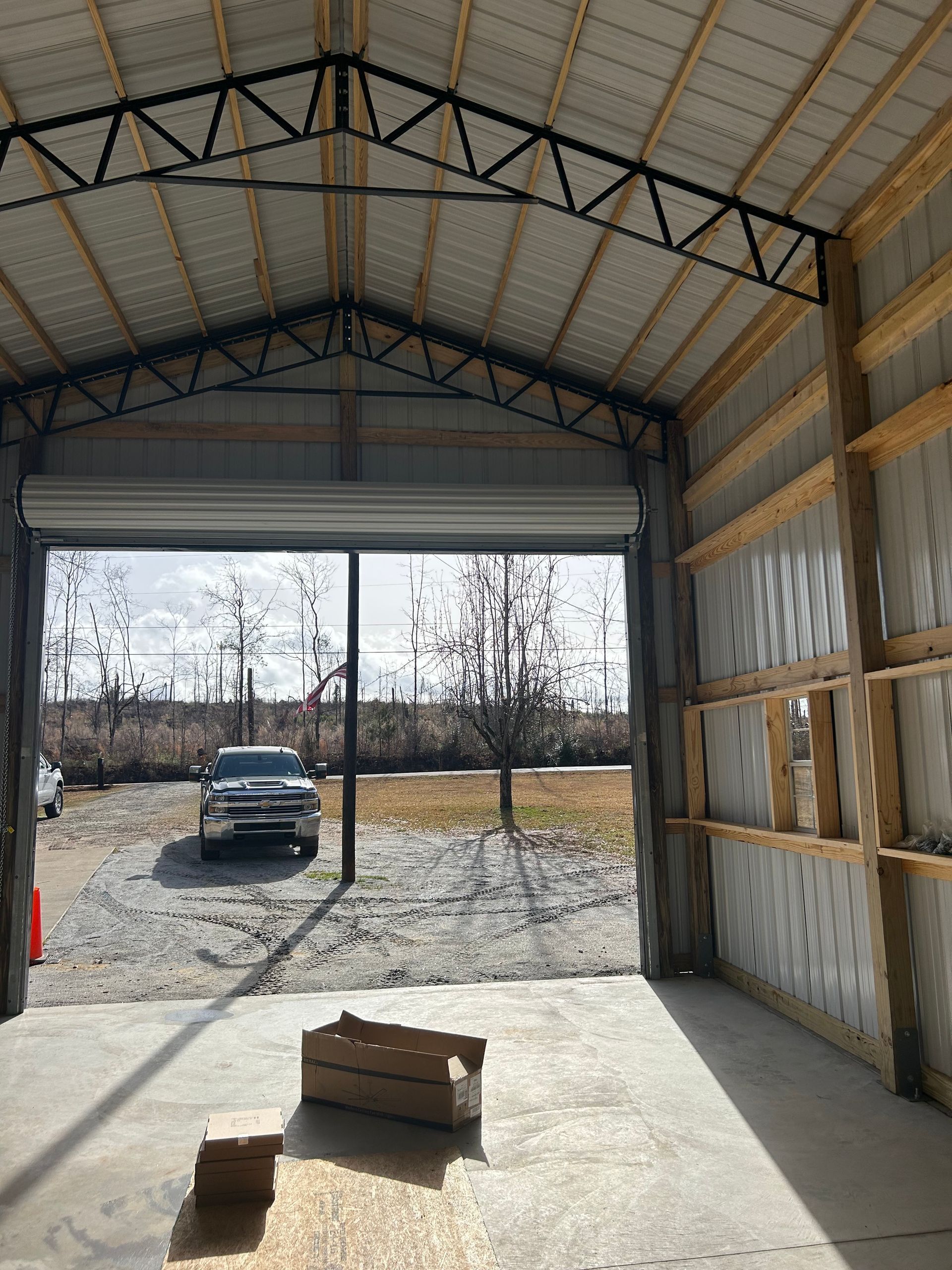 Empty metal garage interior with open door, a truck outside, and materials on the concrete floor