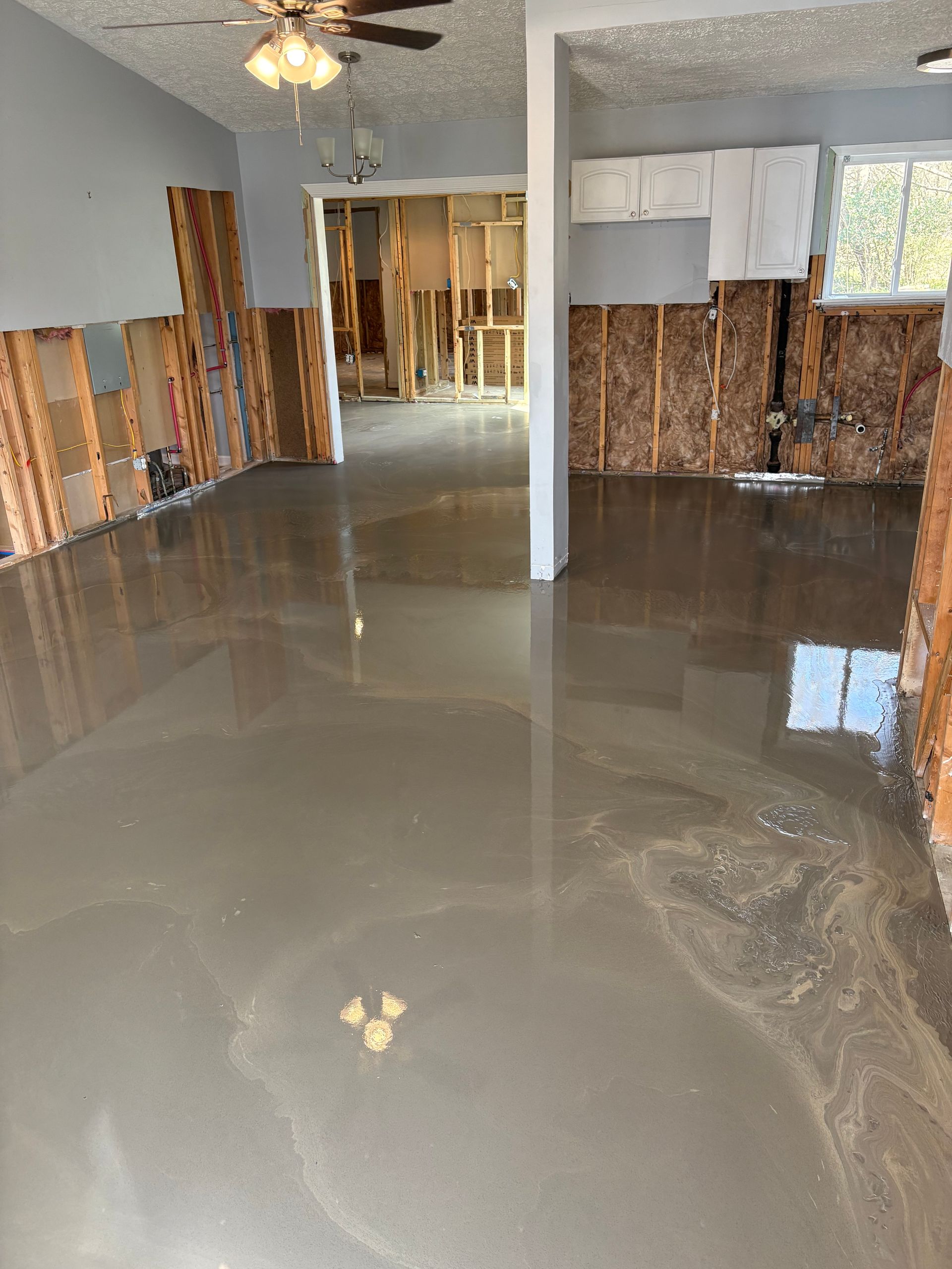 Flooded room with standing water reflecting the ceiling fan and exposed wall studs.