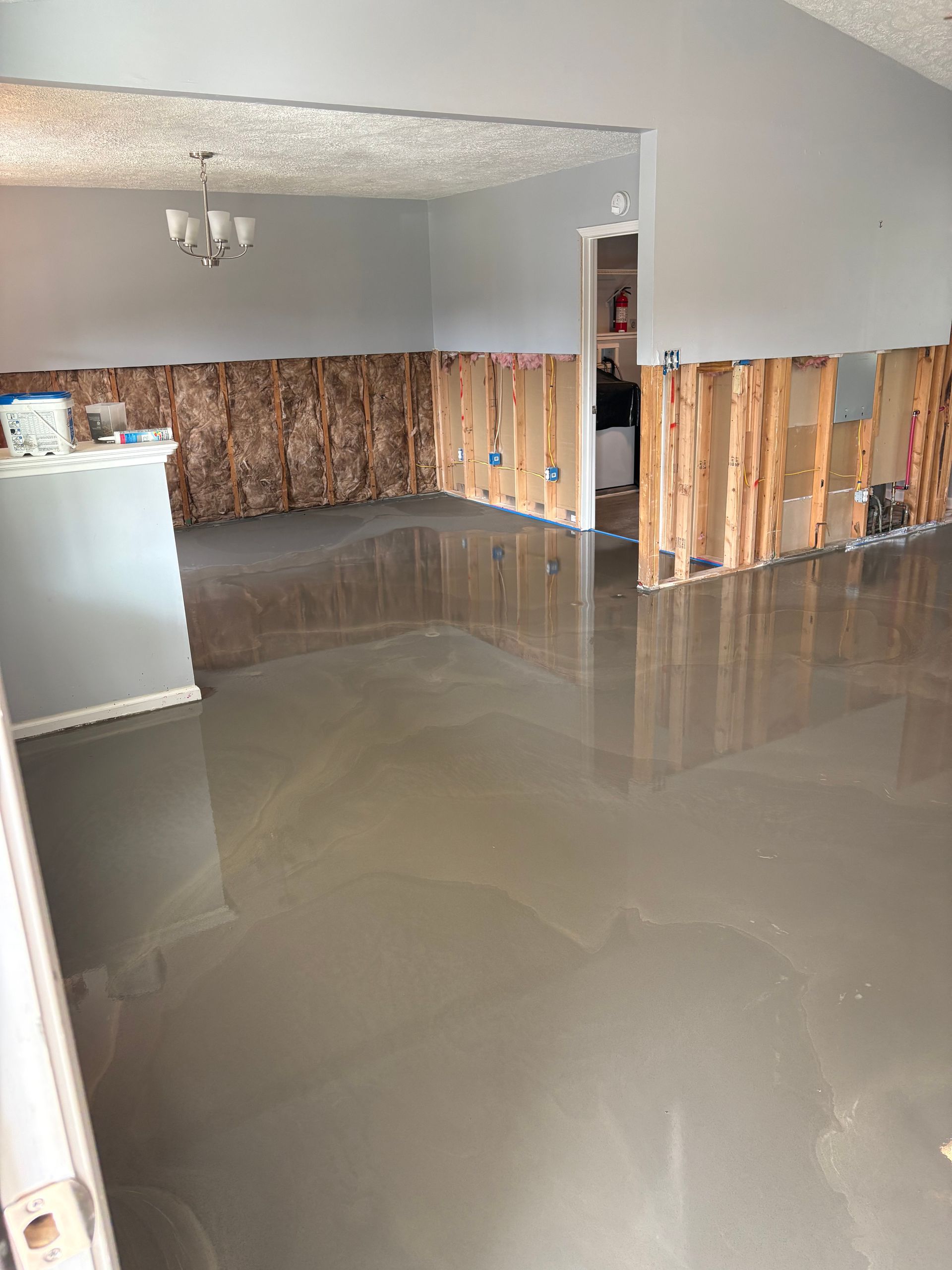 Flooded living room with standing water and damaged lower walls after water intrusion.