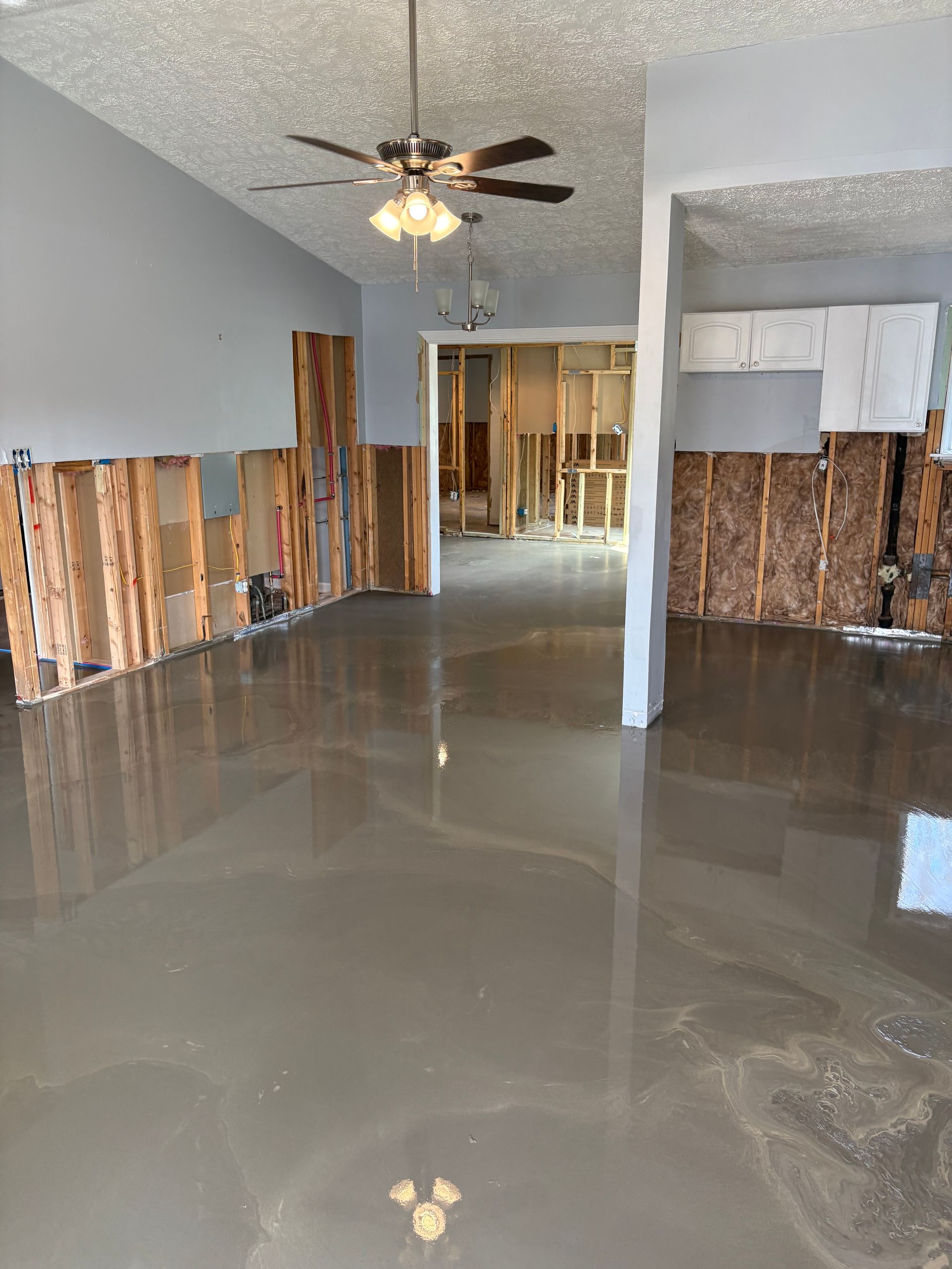 Empty room with glossy floor, exposed lower walls, and ceiling fan under renovation