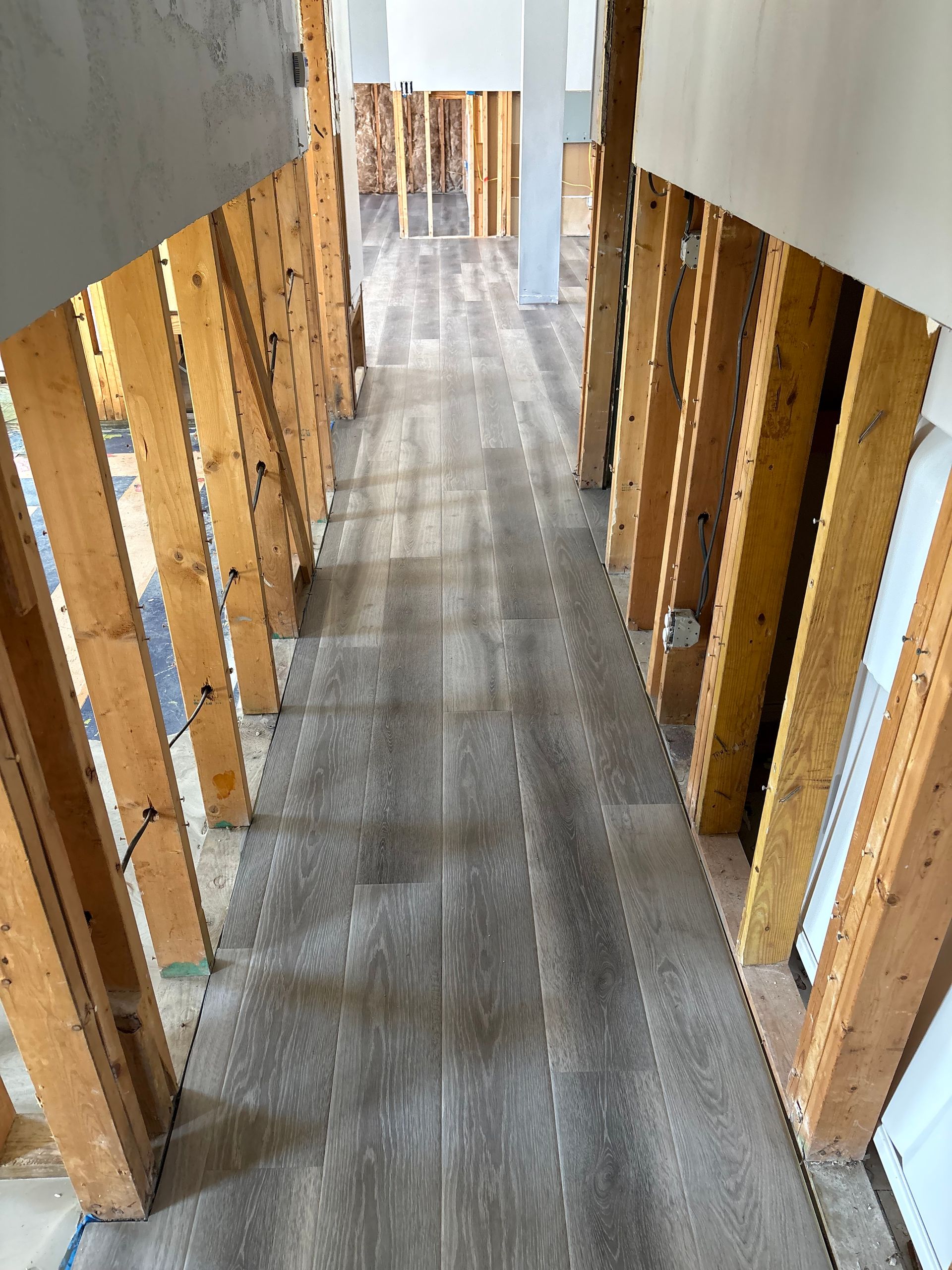 Narrow hallway with exposed wooden studs and gray flooring during renovation