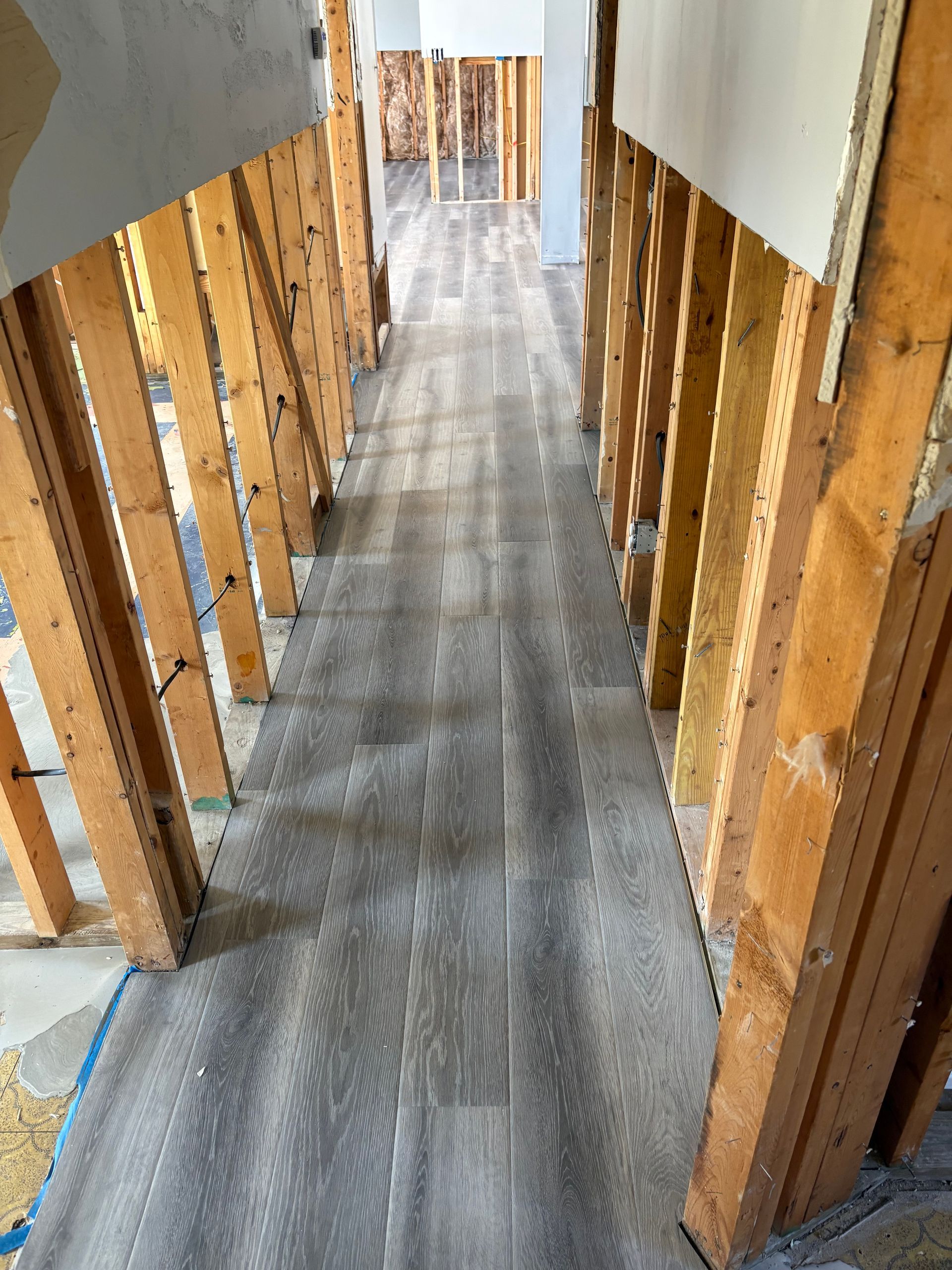 Partially renovated hallway with exposed wall studs and gray flooring, viewed from the center end.