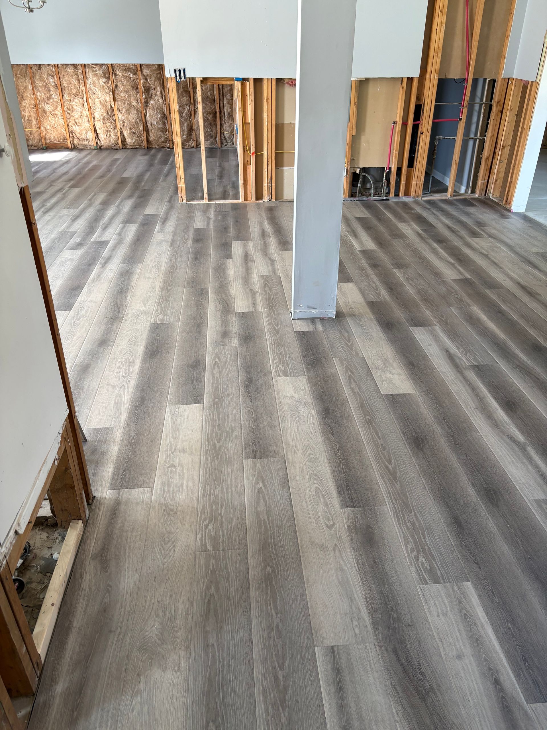 Empty room with gray wood-look flooring, white walls, and exposed framing along the back wall.