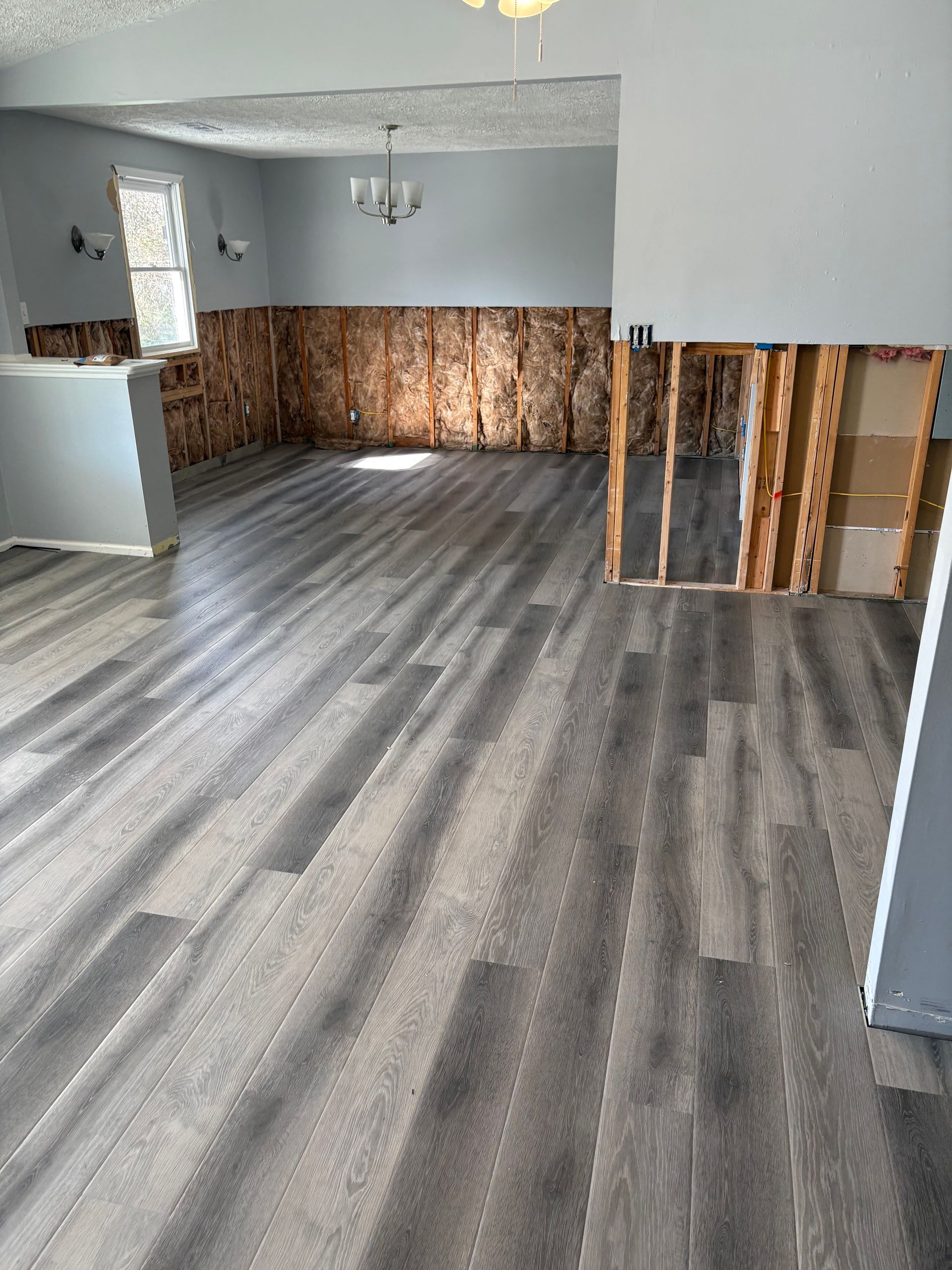 Partially renovated room with gray wood-look flooring and exposed wall studs along one wall