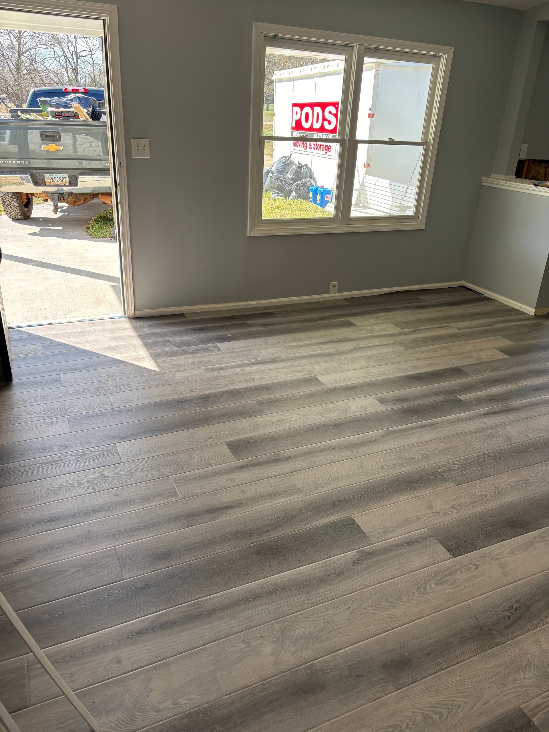 Empty room with gray wood-look flooring and a windowed front entrance, seen from inside