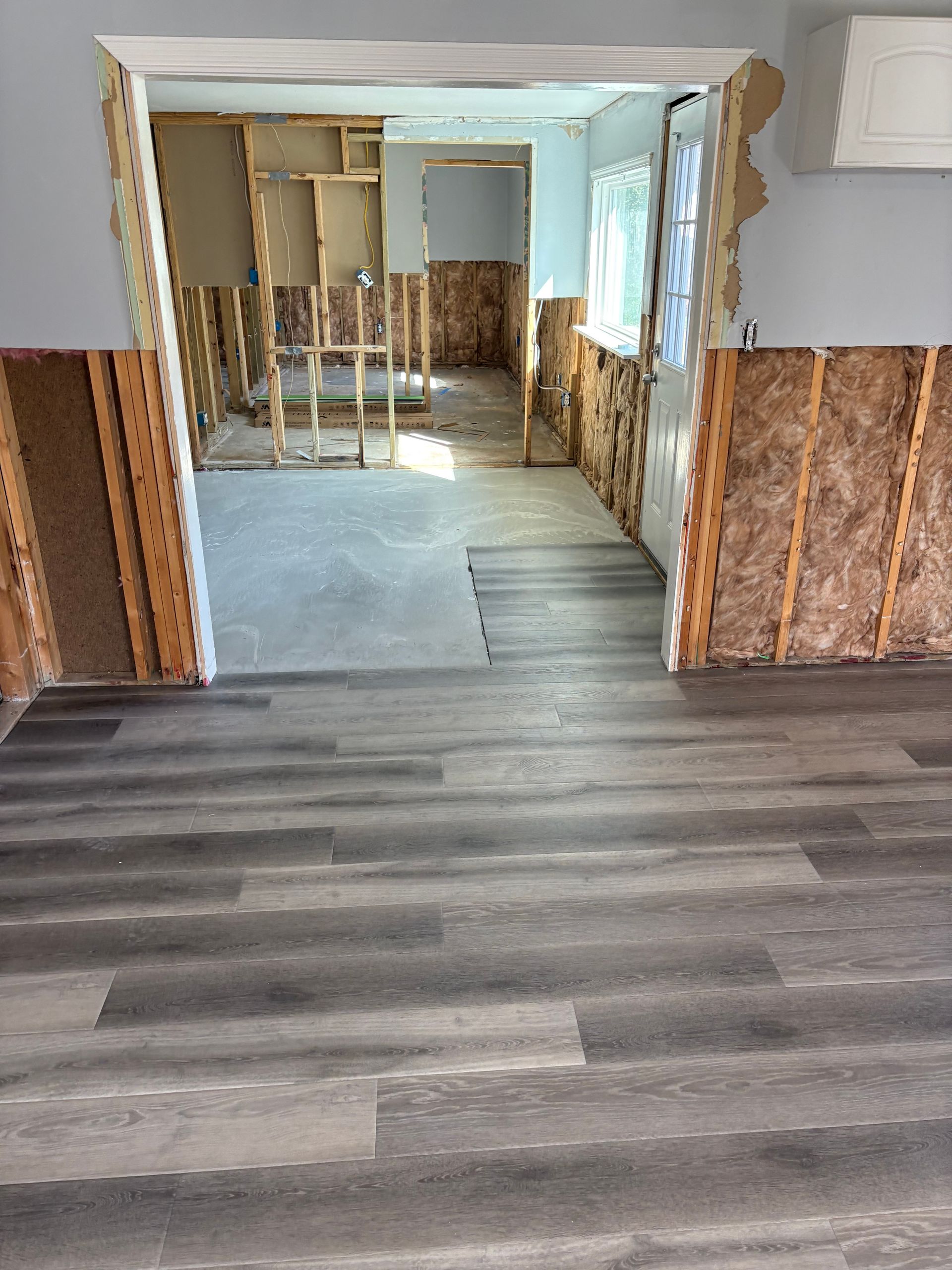 Renovated room with gray wood-look flooring leading into a partially gutted interior space